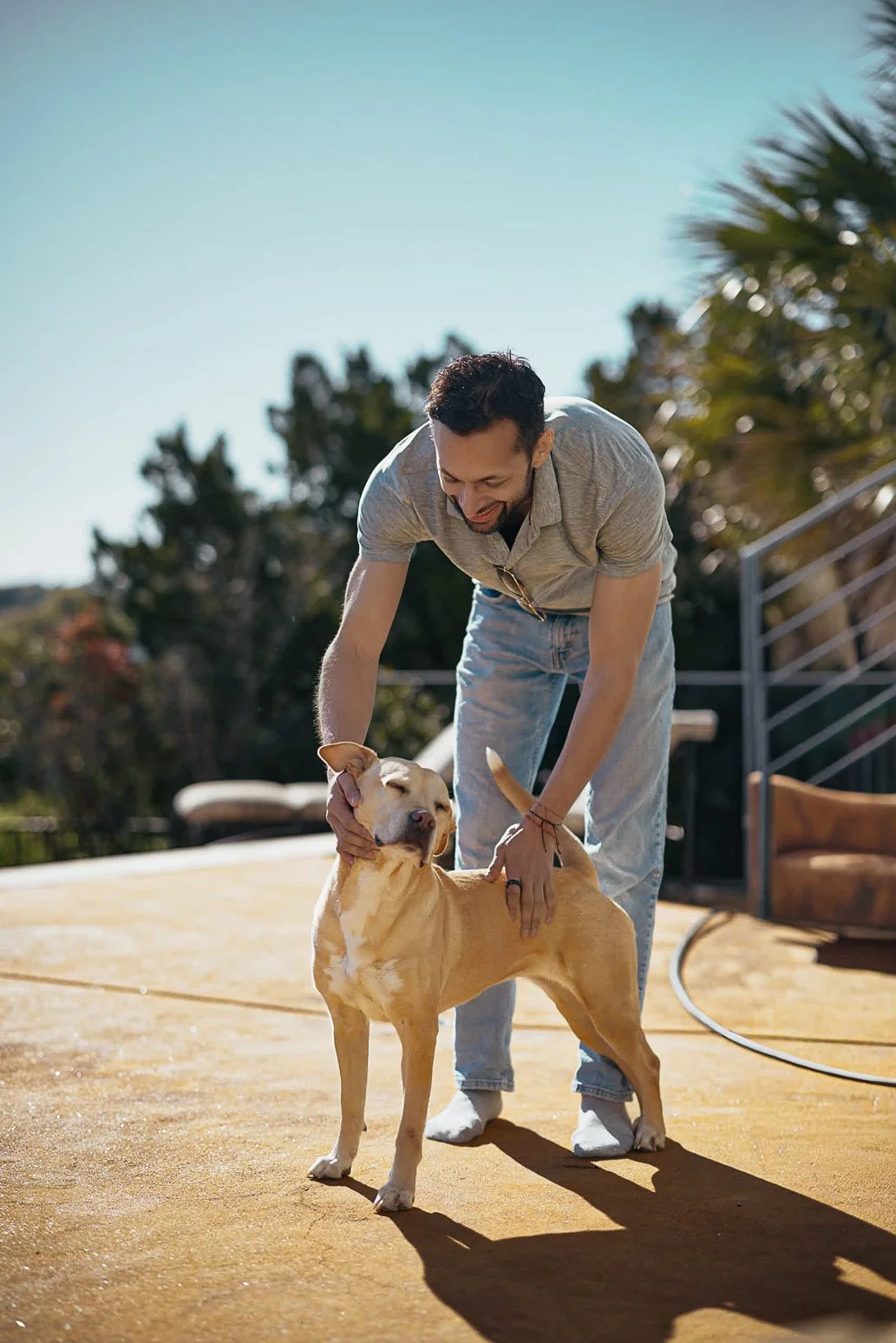 Man smiling with a his dog, next to the pool, a fun moment with him petting the dog from an Austin dating photography session