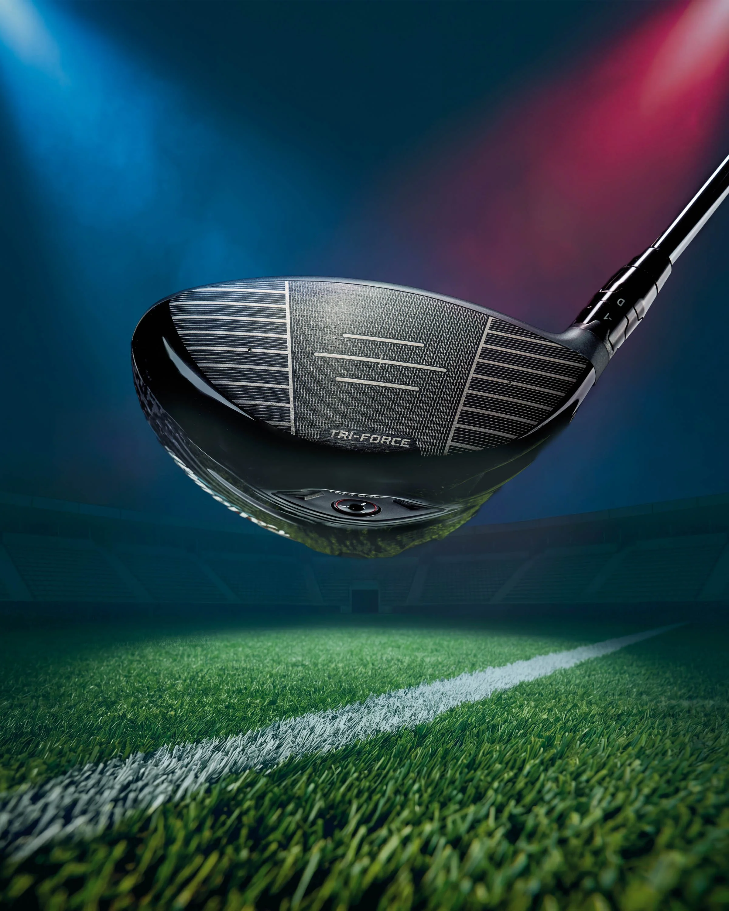 Close-up of a golf club on a golf course with greenery and stadium lights in the background.