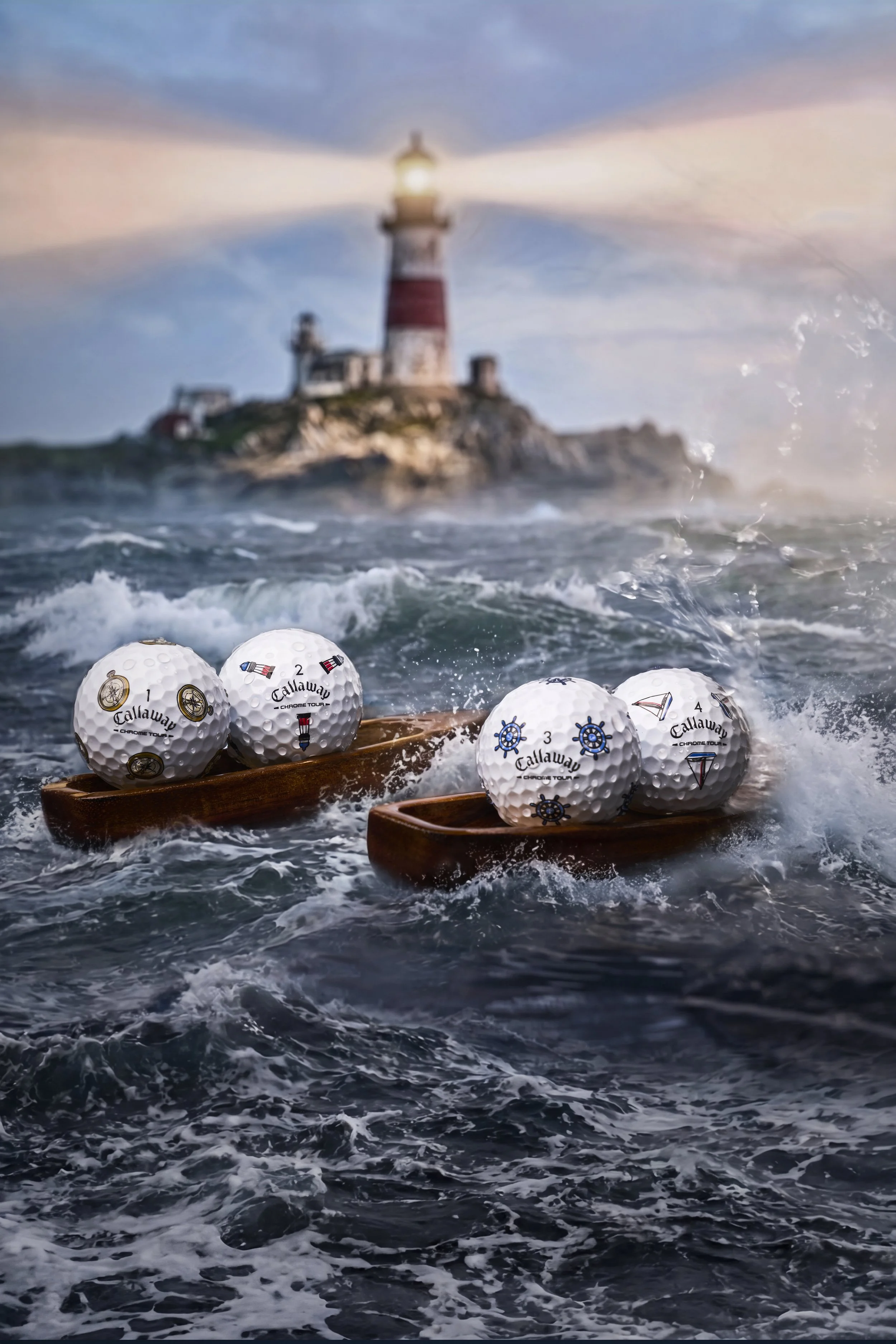 Several white Callaway golf balls with nautical and racing designs floating on the surface of the water near two wooden boats. A blurred lighthouse is in the background with waves crashing around.
