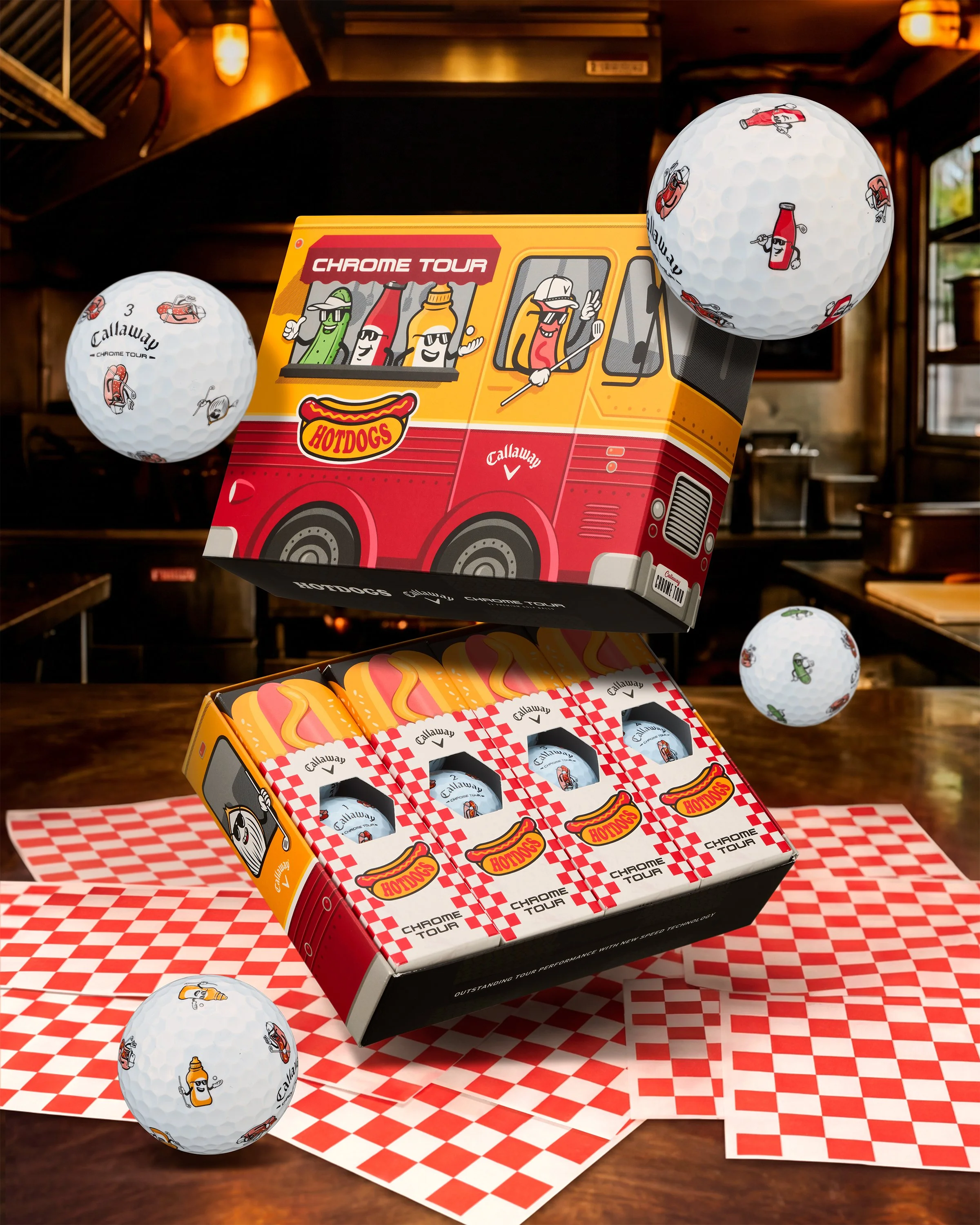Several golf balls with cartoon condiment illustrations, a yellow and red box of Callaway Chrome Tour golf balls, and a matching red and white checkered paper on a wooden table.
