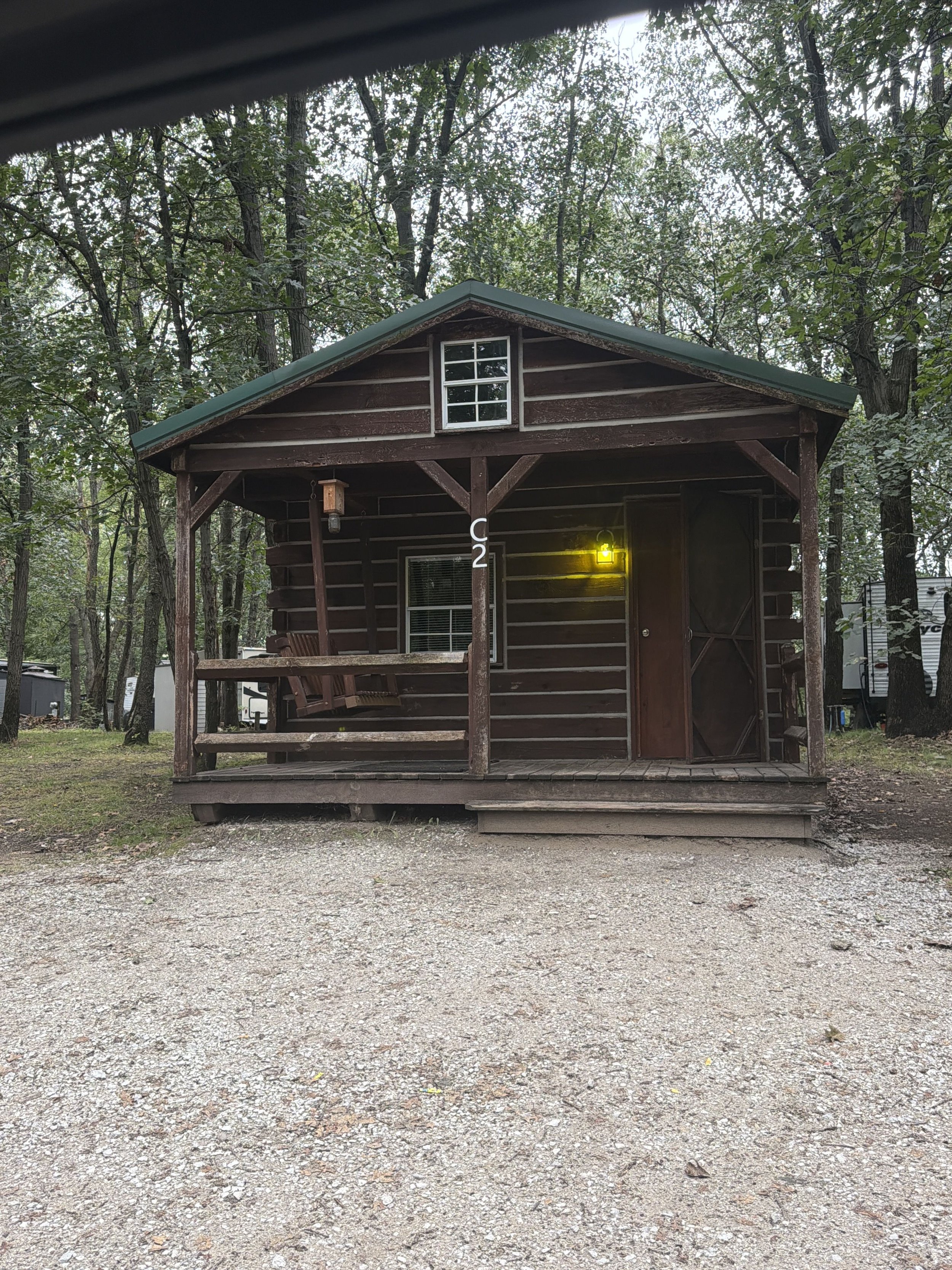 A cabin with a porch & window and a loft window upstairs.