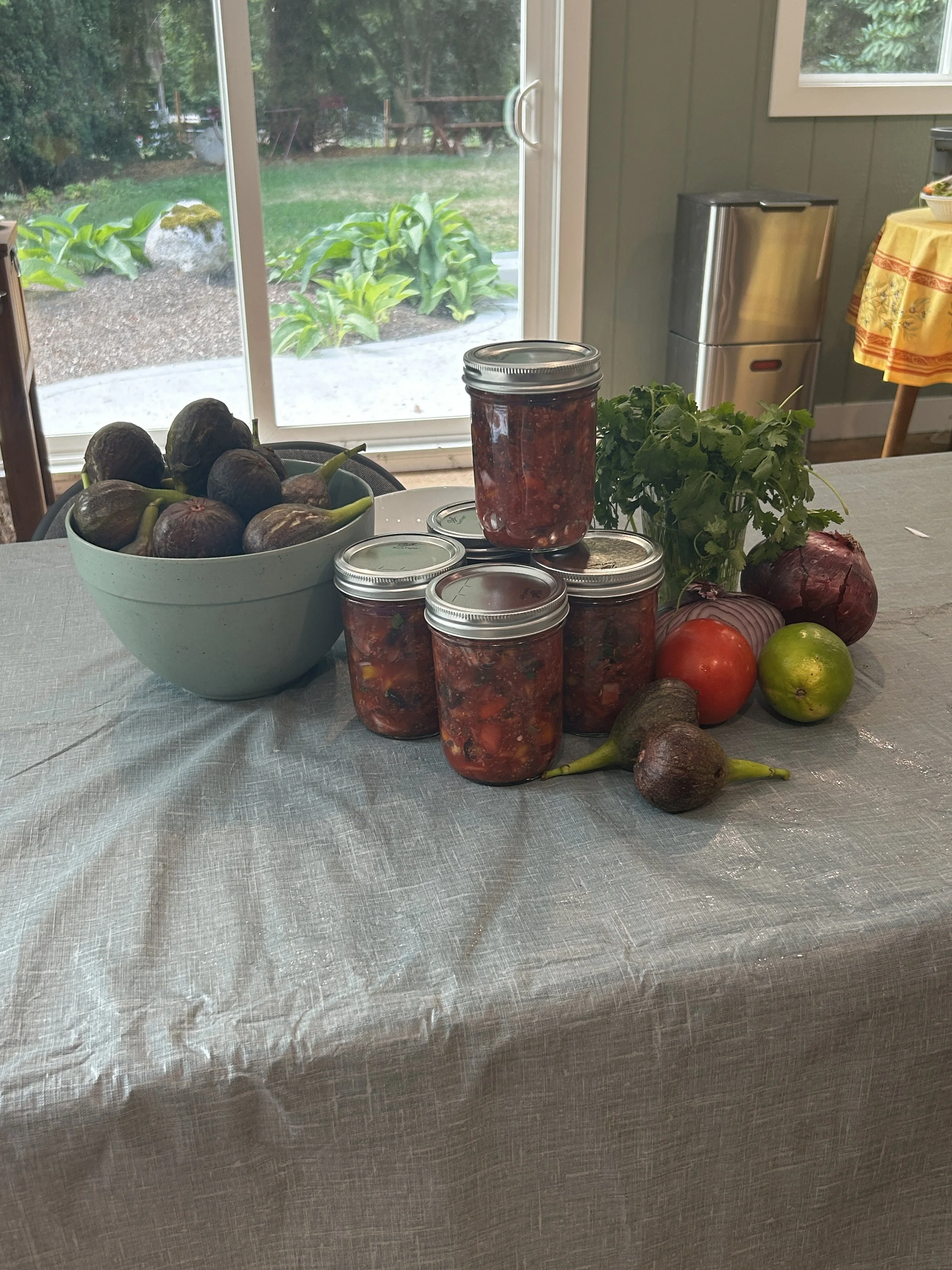 A bowl of figs sits next to five jars of fig salsa and other produce