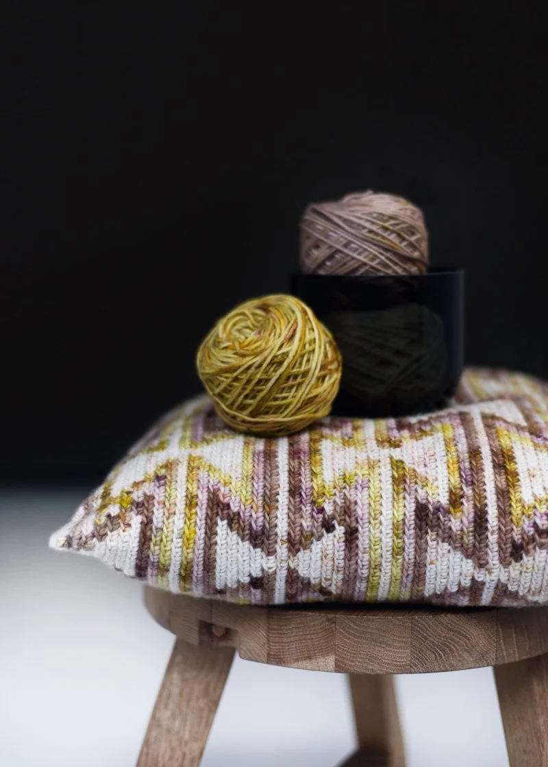 Crocheted cushion with traditional Wayuu tribe pattern displayed on a Tom Dixon wooden stool with ball of yarn