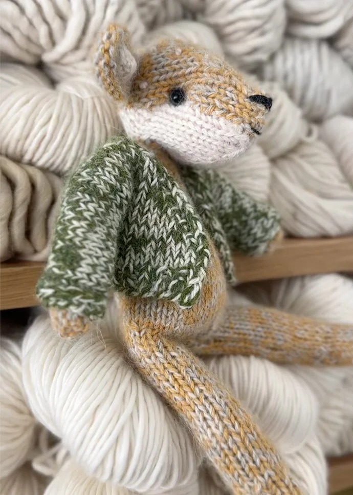 Handmade knitted rabbit by Dot Pebbles Knit sitting on a pile of natural yarn, knitting pattern included in KOEL