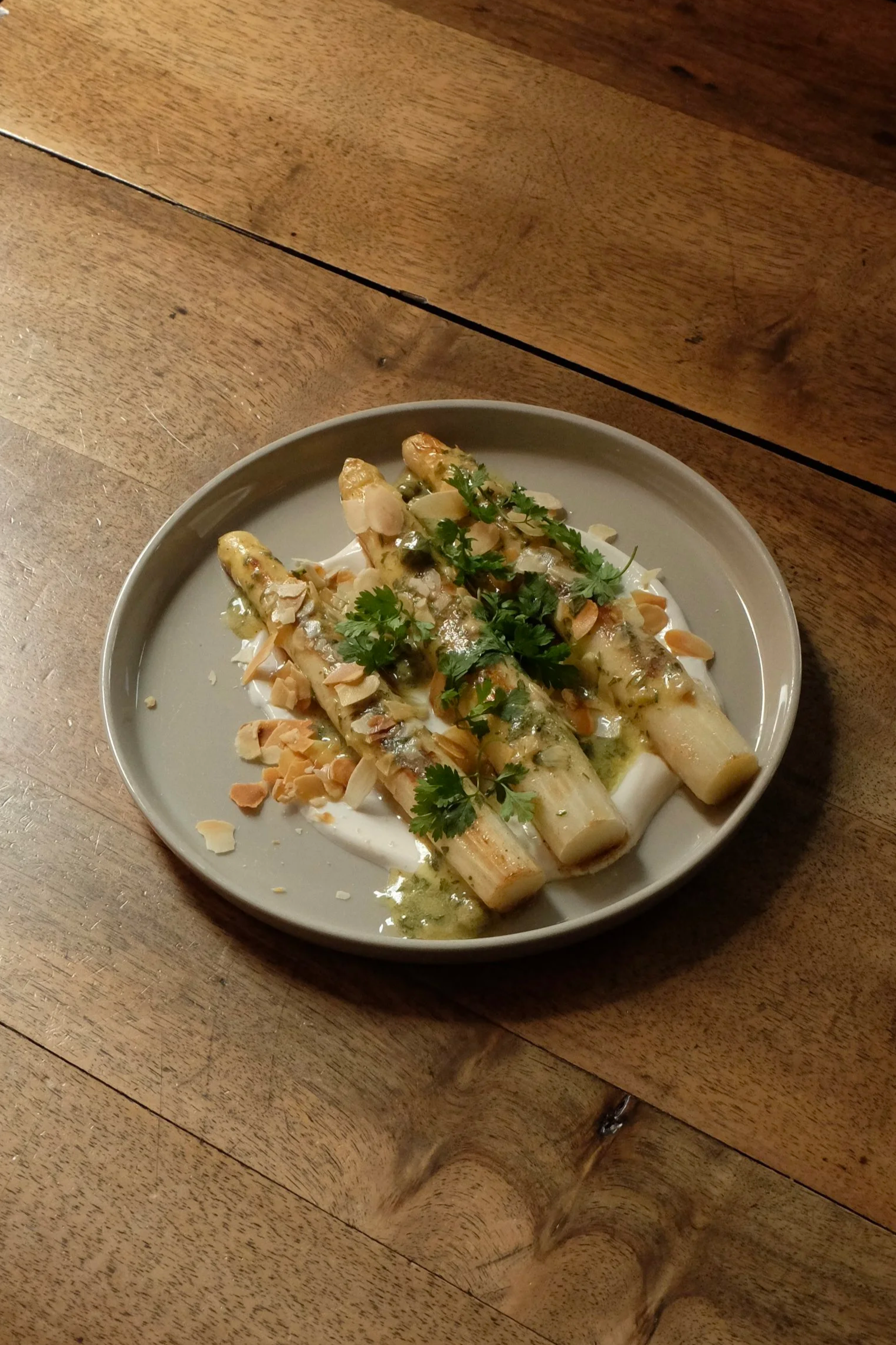Assiette de légumes grillés garnie de coriandre, d'amandes effilées et arrosée d'une sauce verte, placée sur une table en bois.