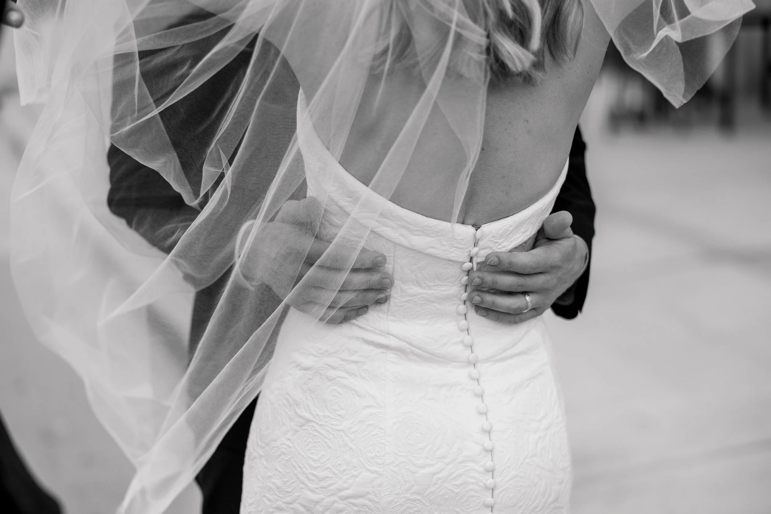 Close-up of a Green Bay wedding couple embracing at a wedding, with one person wearing a white lace wedding dress and the other in a dark suit, holding each other.