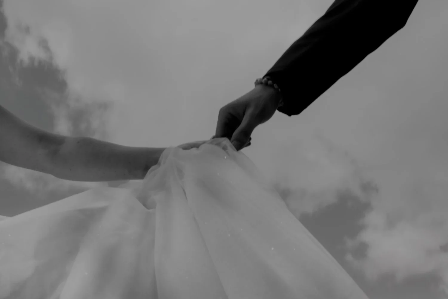 A couple holding hands, with the bride in a white wedding dress and veil, against a cloudy sky in Appleton, Wisconsin.