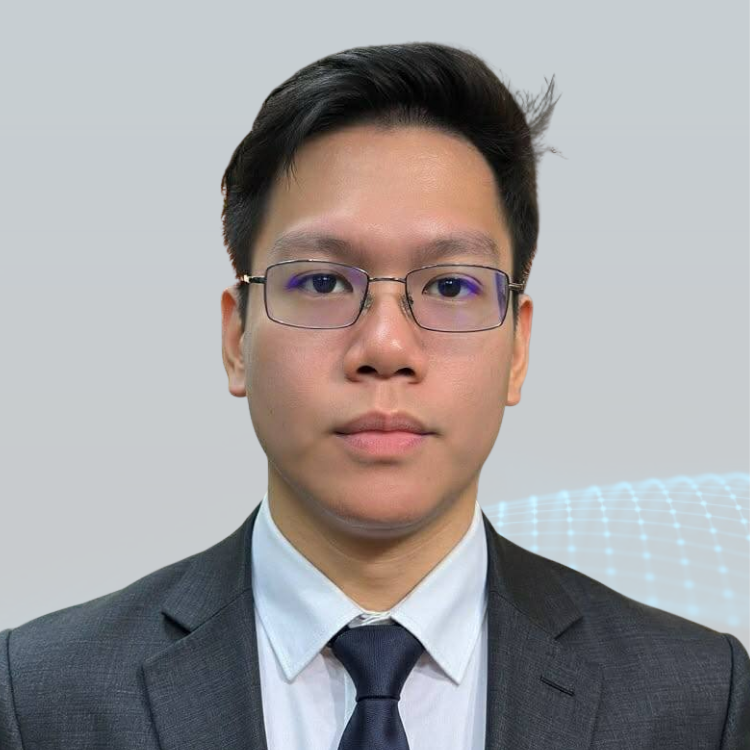 A young man with glasses, wearing a suit and tie, posing against a plain gray background.