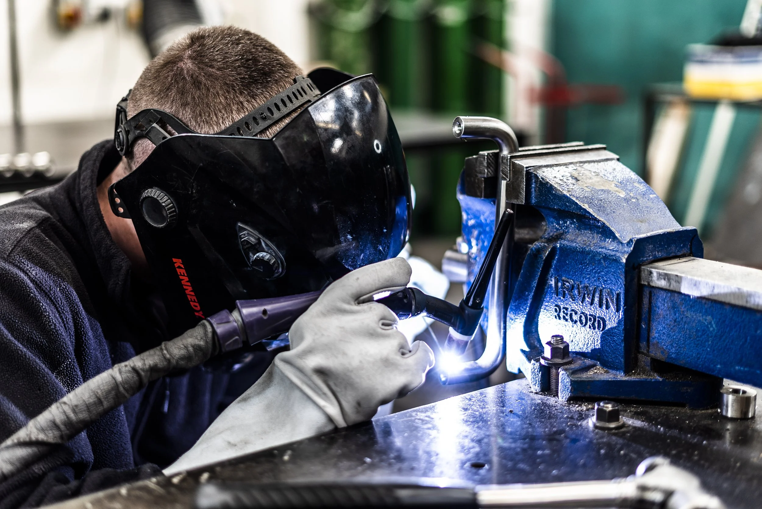 A person welding metal using a welding machine, wearing safety goggles and gloves, in a workshop.