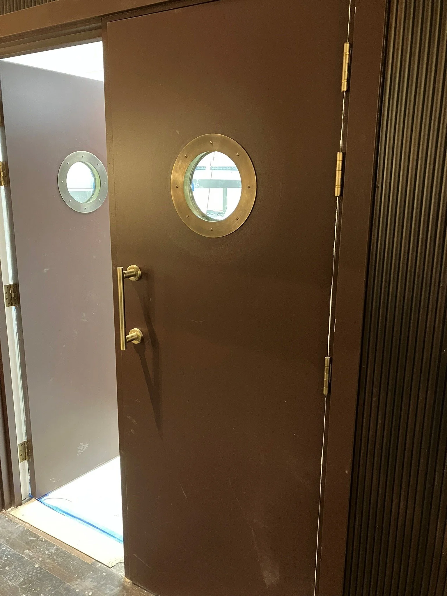 Brown door with round porthole windows, one large and one small, and a silver door handle.
