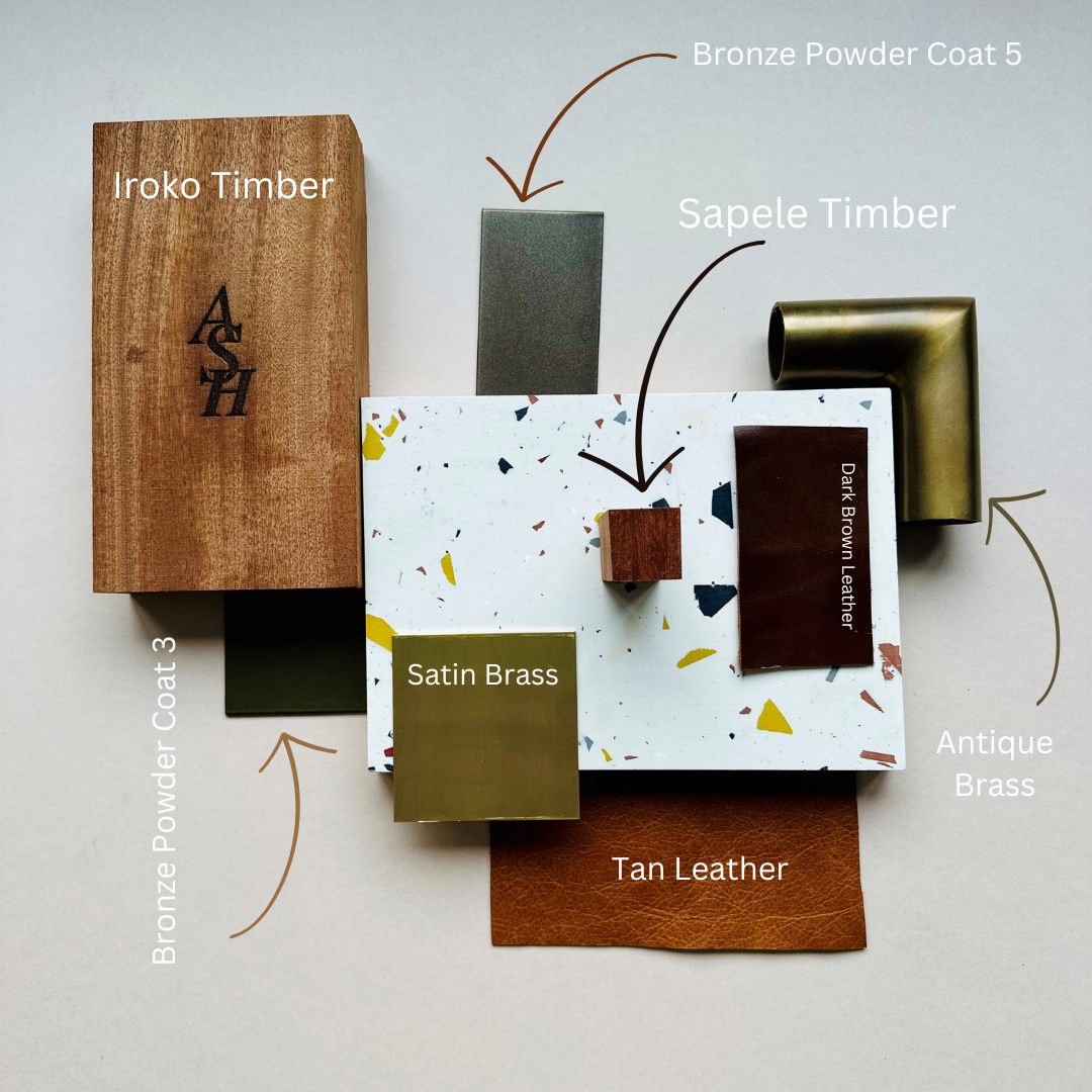 Sample material swatches labeled with names and descriptions, including a piece of Iroko timber with initials A and H, a bronze powder coat 3, satin brass, tan leather, a dark brown leather, a bronze powder coat 5, and an antique brass corner piece.