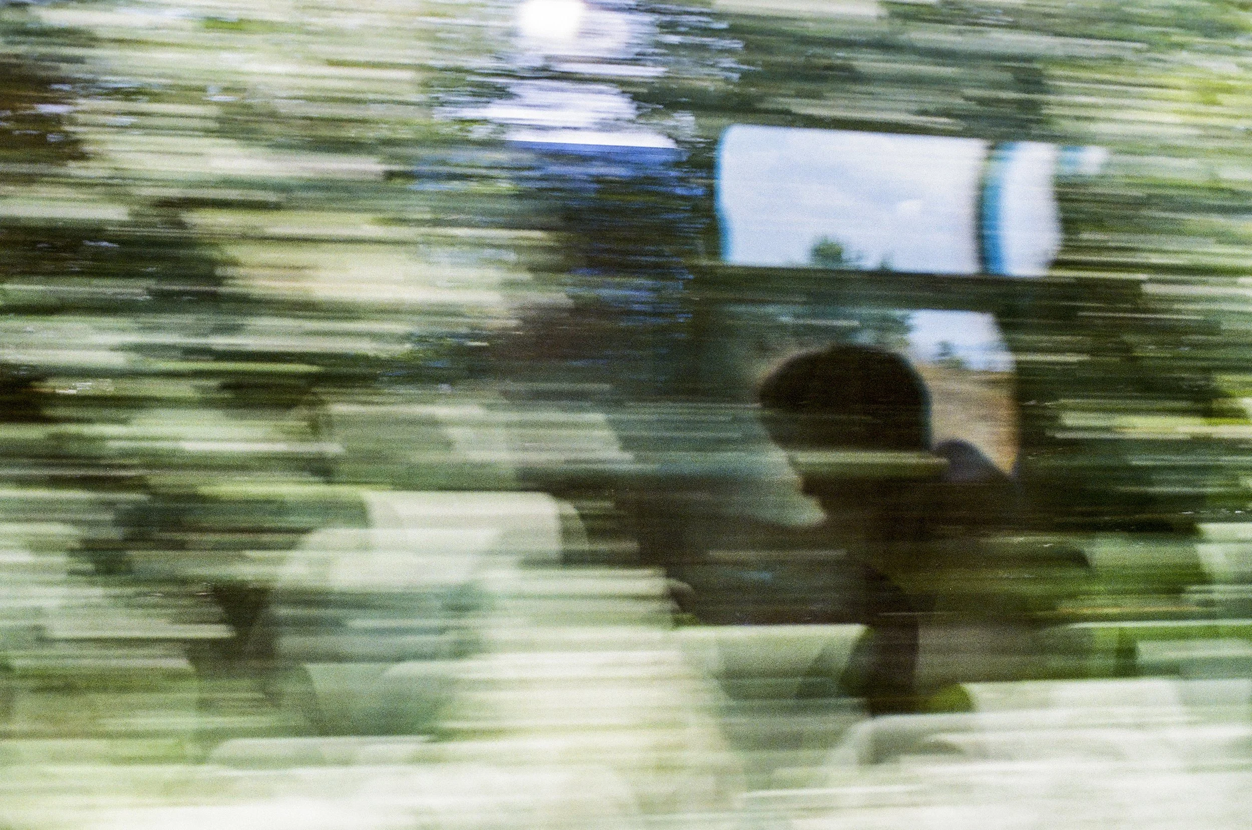 A blurry photo taken in motion showing a person taking a selfie in a car mirror with trees and sky in the background.