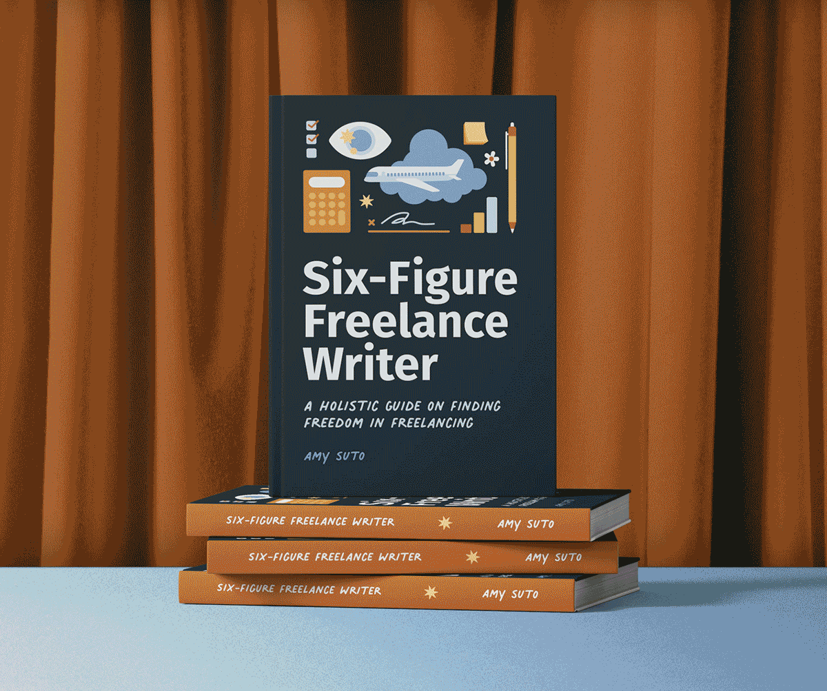 A copy of the book titled 'Six-Figure Freelance Writer' by Amy Suto is standing upright on a stack of three identical books with the same title and author, placed on a white surface against a curtain background.