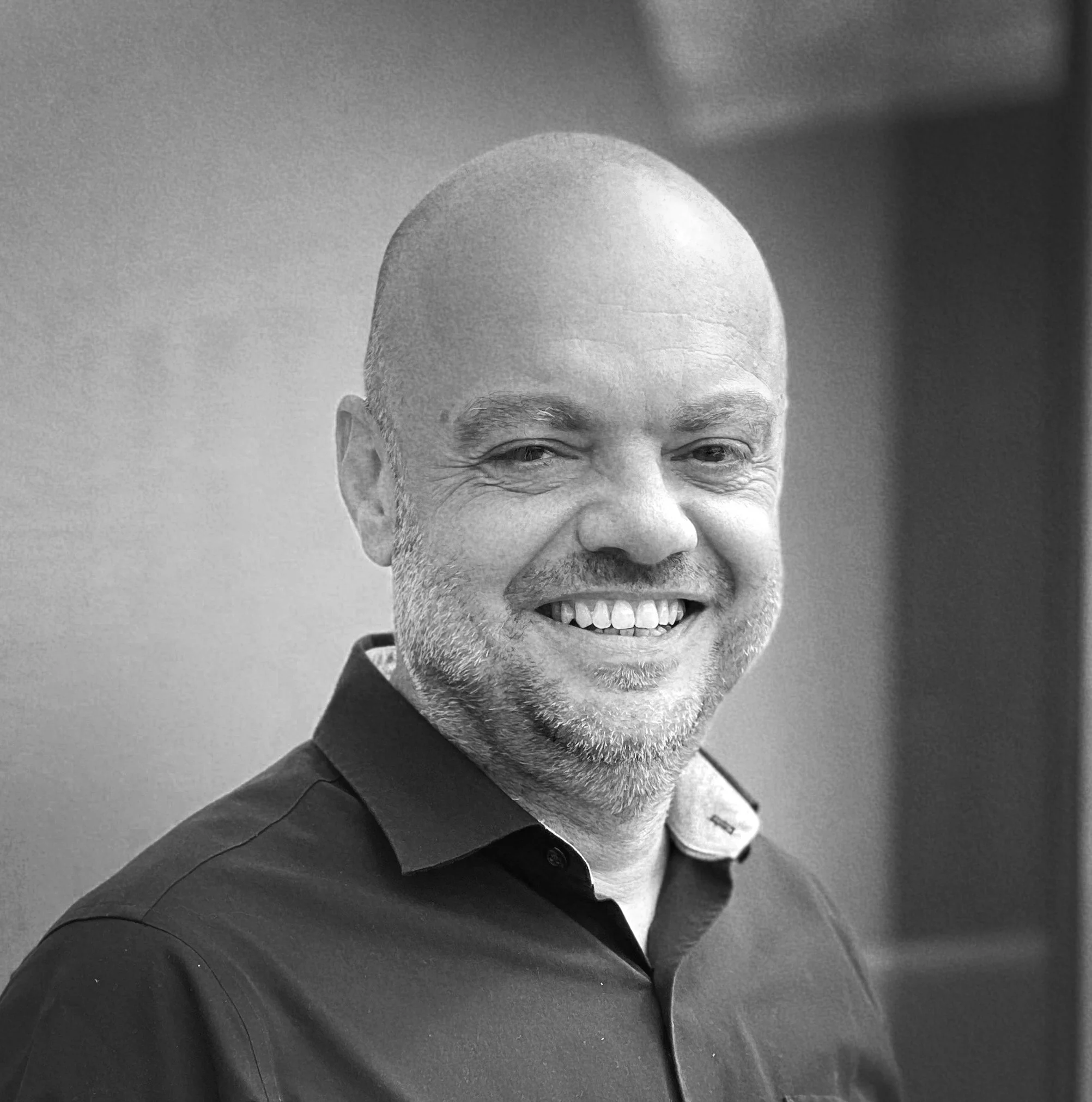 Smiling bald man with a beard wearing a dark blue shirt against a blue background.
