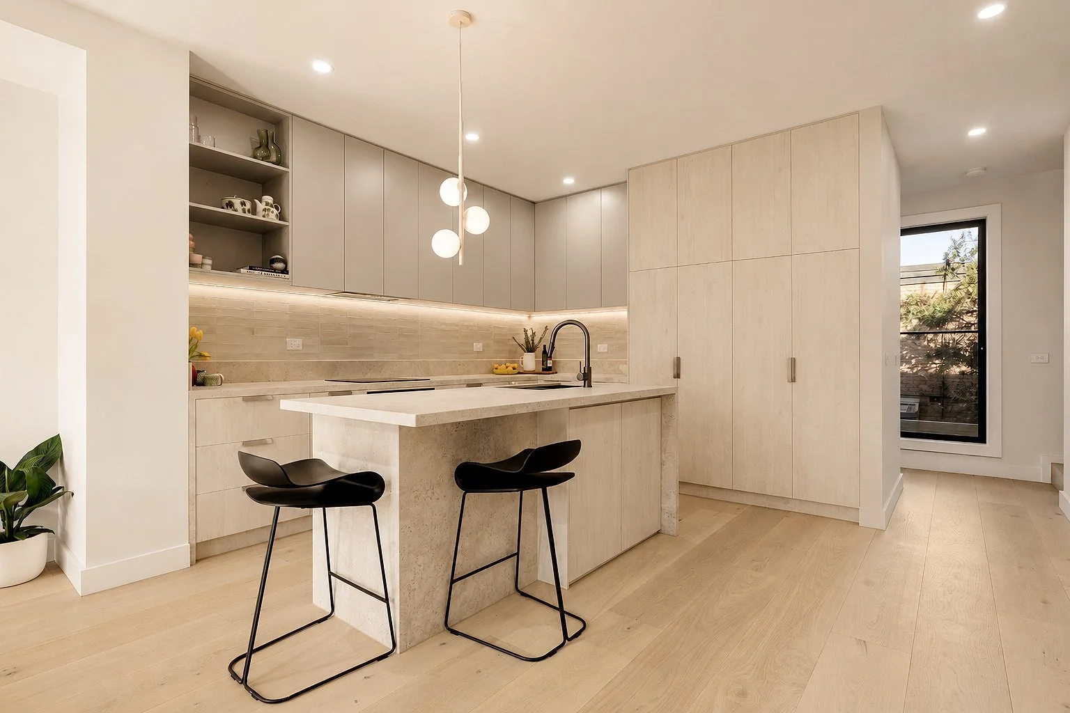 Modern kitchen with light wood cabinets, a beige tile backsplash, black bar stools, and a white stone kitchen island with a sink.
