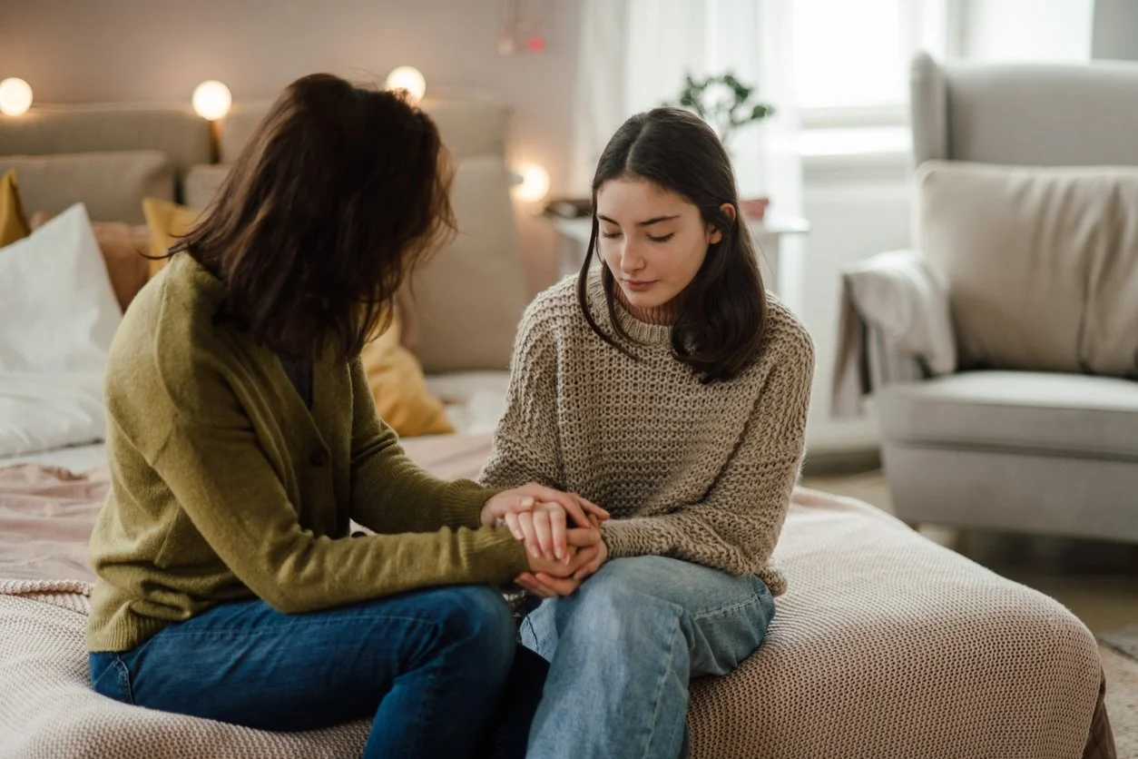 A concerned mother holding her daughter’s hands on a bed, symbolizing emotional support and the importance of legal help in child custody cases.