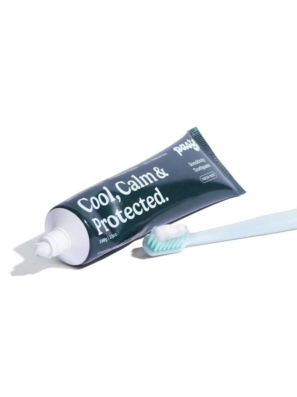 The extra soft bristle manual toothbrush laid down on a plain surface with toothpaste on the bristles with the mint anti-sensitivity toothpaste next to it.