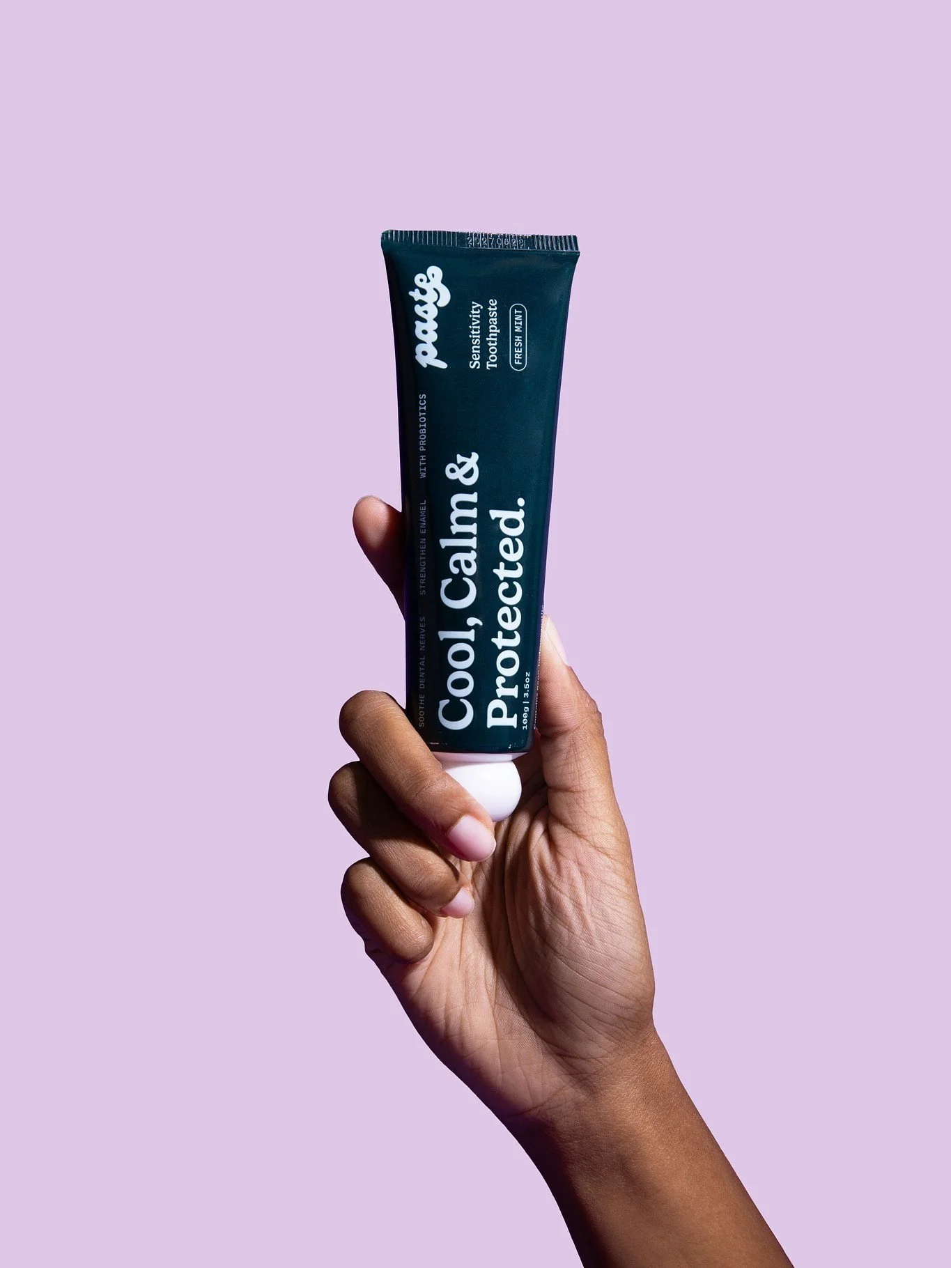 A hand holding a tube of the mint anti-sensitivity toothpaste with a violet background.