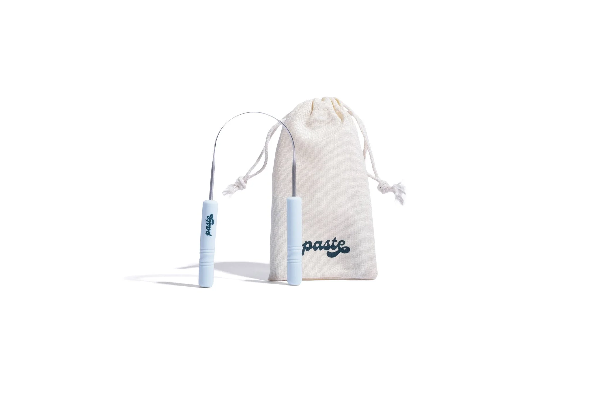 The tongue scraper standing upright next to a Paste-branded pouch.