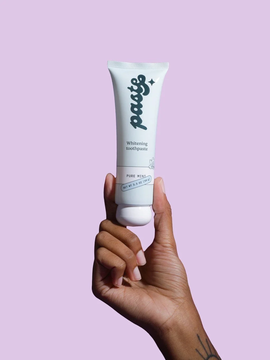 A hand holding a tube of the mint whitening toothpaste with a violet background.
