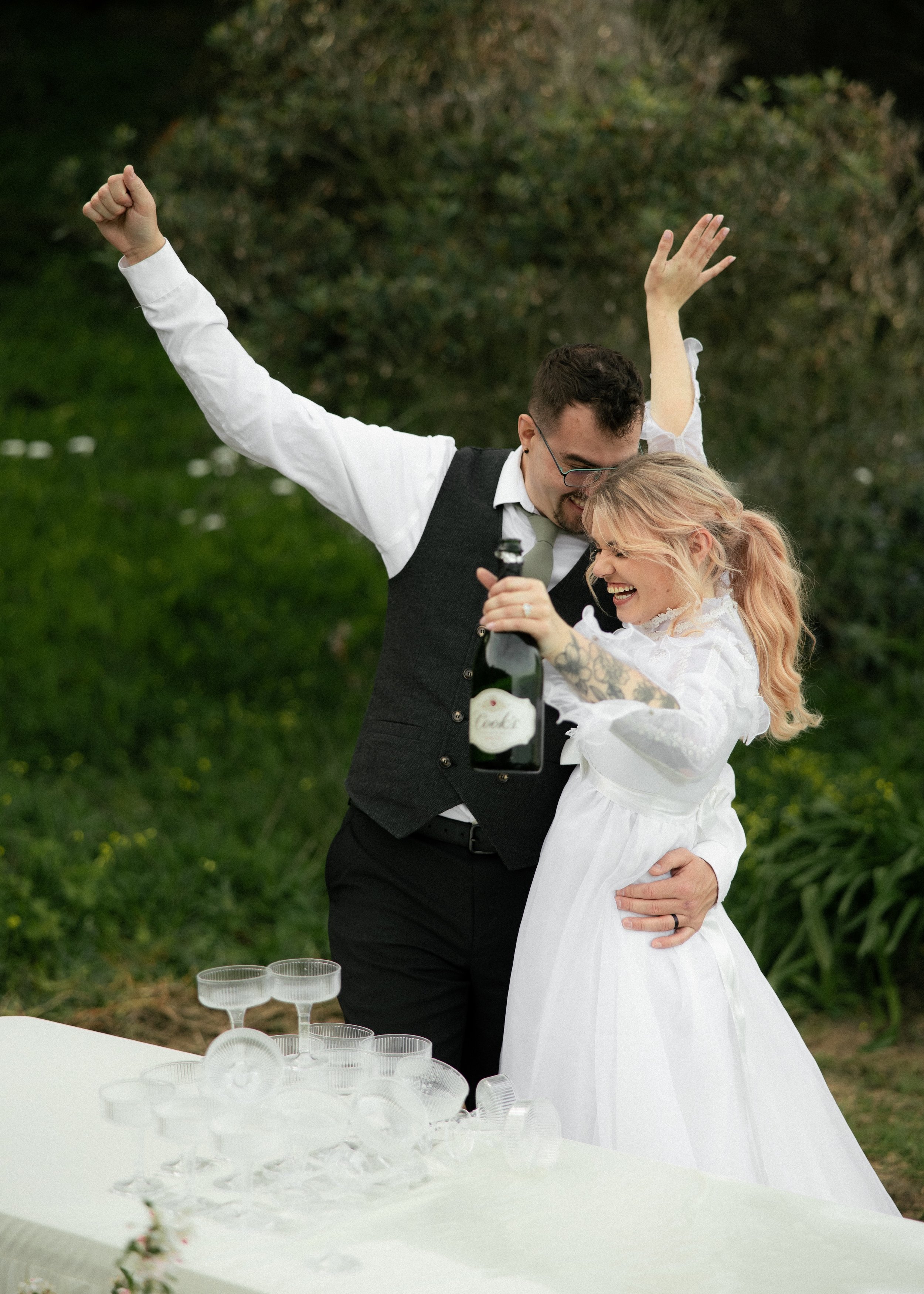 Couple holding a bottle of champagne in front of a set of champagne glasses celebrating being married