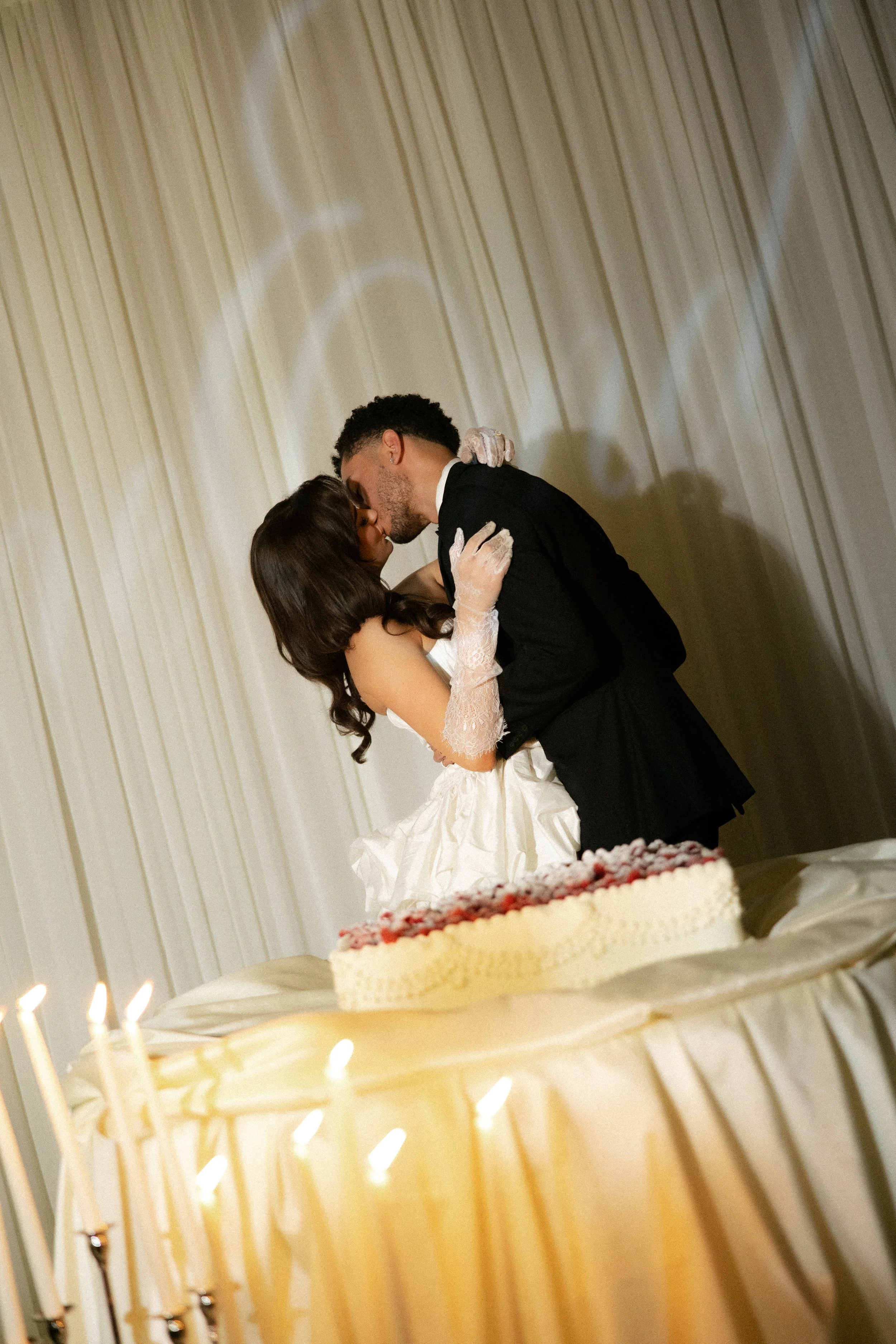 bride and groom in front of a wedding cake in elegant editorial outfits kissing