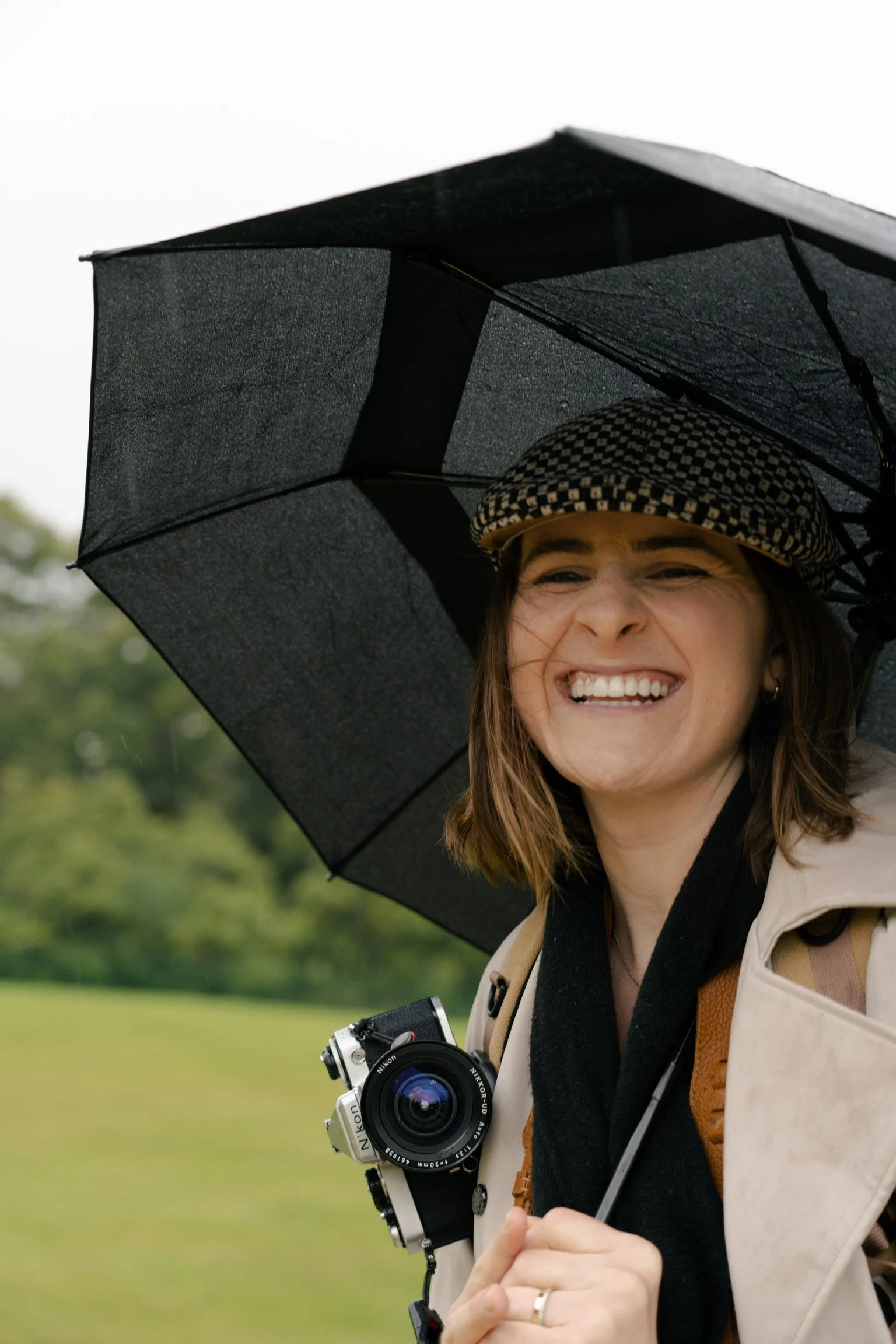 Photo of a girl smiling at the camera, under a black umbrella holding a film camera