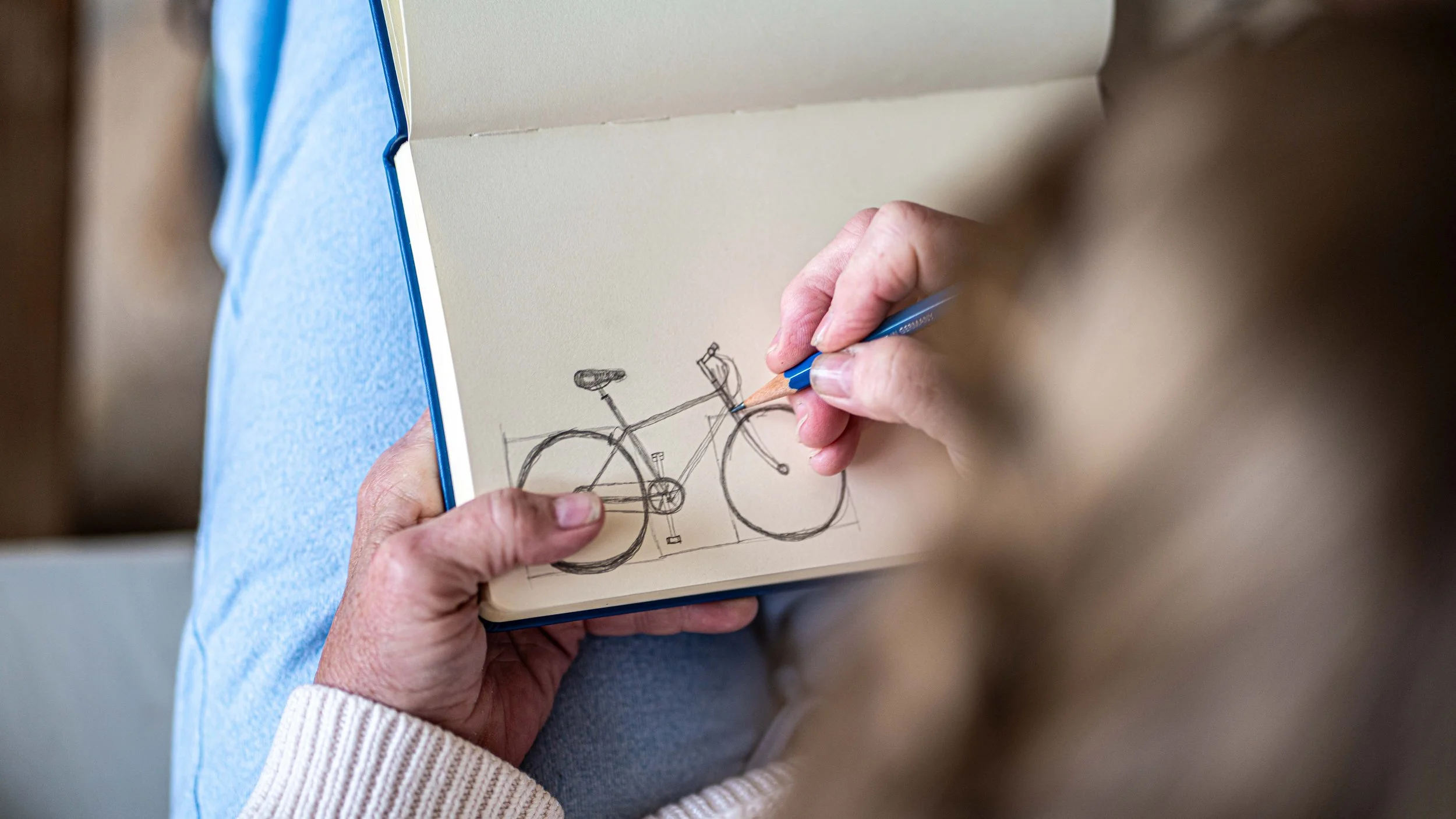 Person sketching a bicycle in a notebook with a pencil.