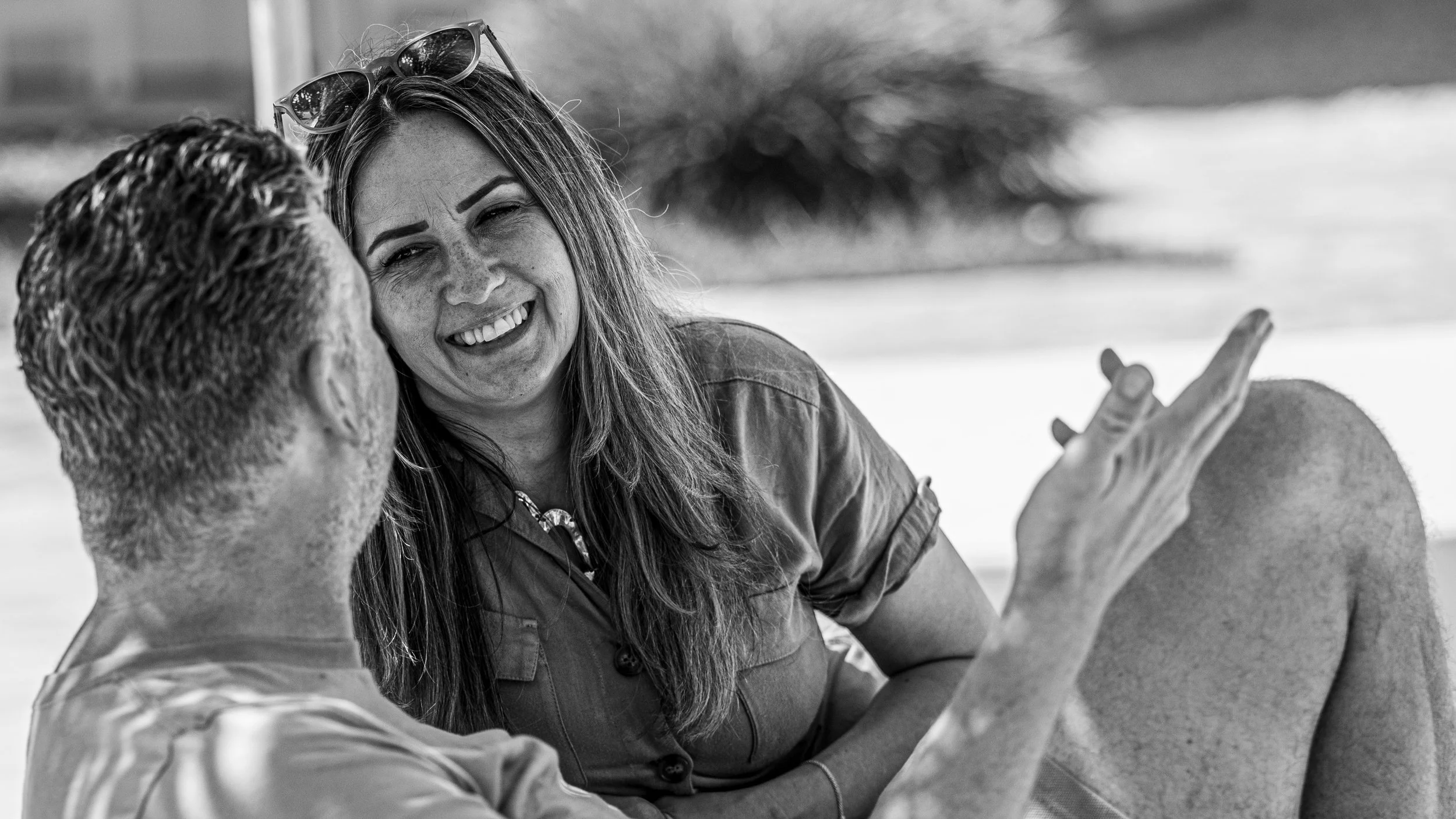 A woman smiling and talking to a man outdoors on a sunny day.