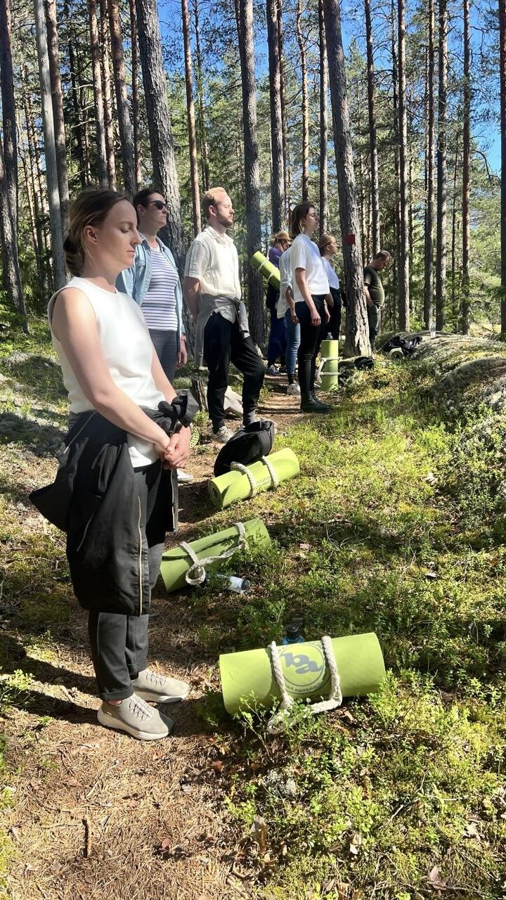 Yritysryhmä seisoo metsässä kuuntelemassa luonnon ääniä