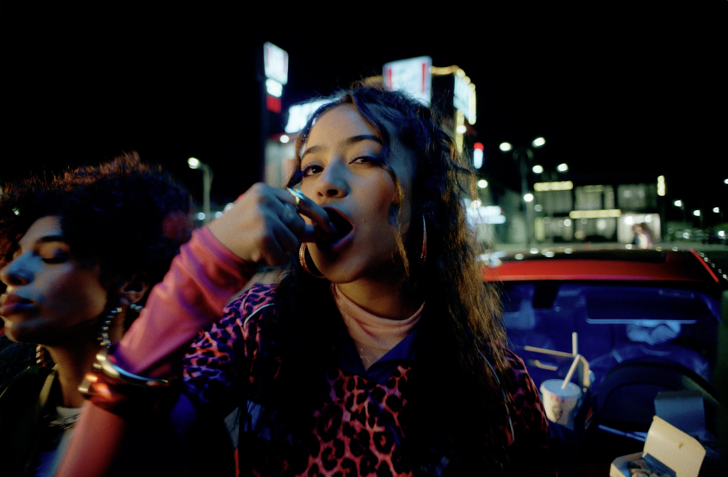 Woman eating KFC outside a restaurant at night in a commercial still, cinematography by Johan-Fredrik Bødtker.