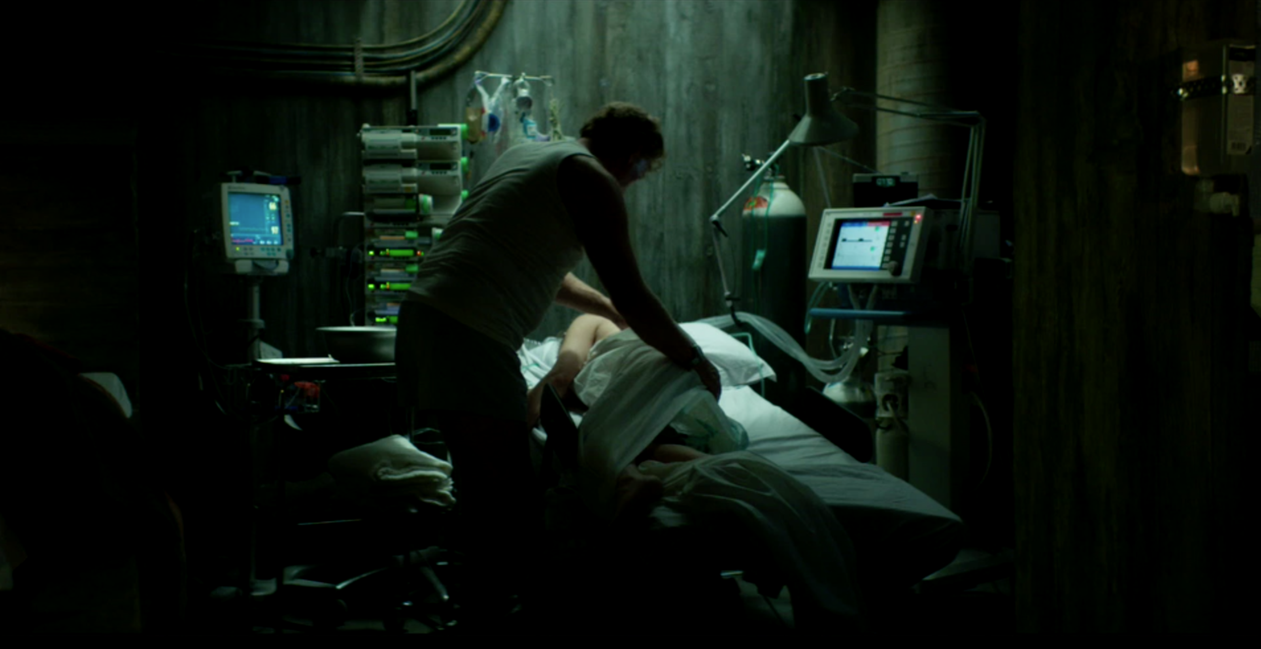Man treating a patient in a dark underground medical room in Valkyrien, cinematography by Johan-Fredrik Bødtker.