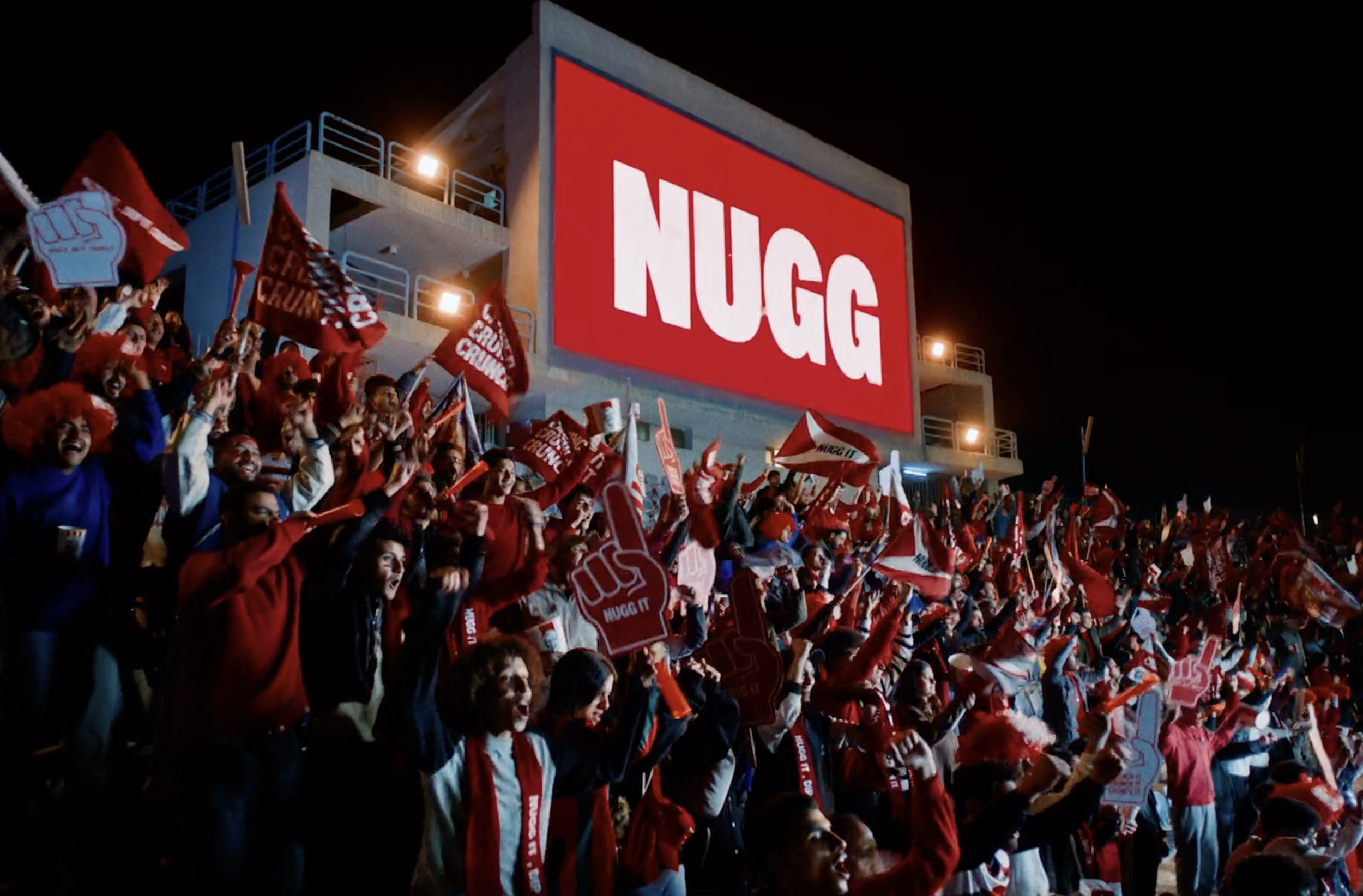 Crowd of football fans celebrating beneath a NUGG sign in a KFC commercial, cinematography by Johan-Fredrik Bødtker.