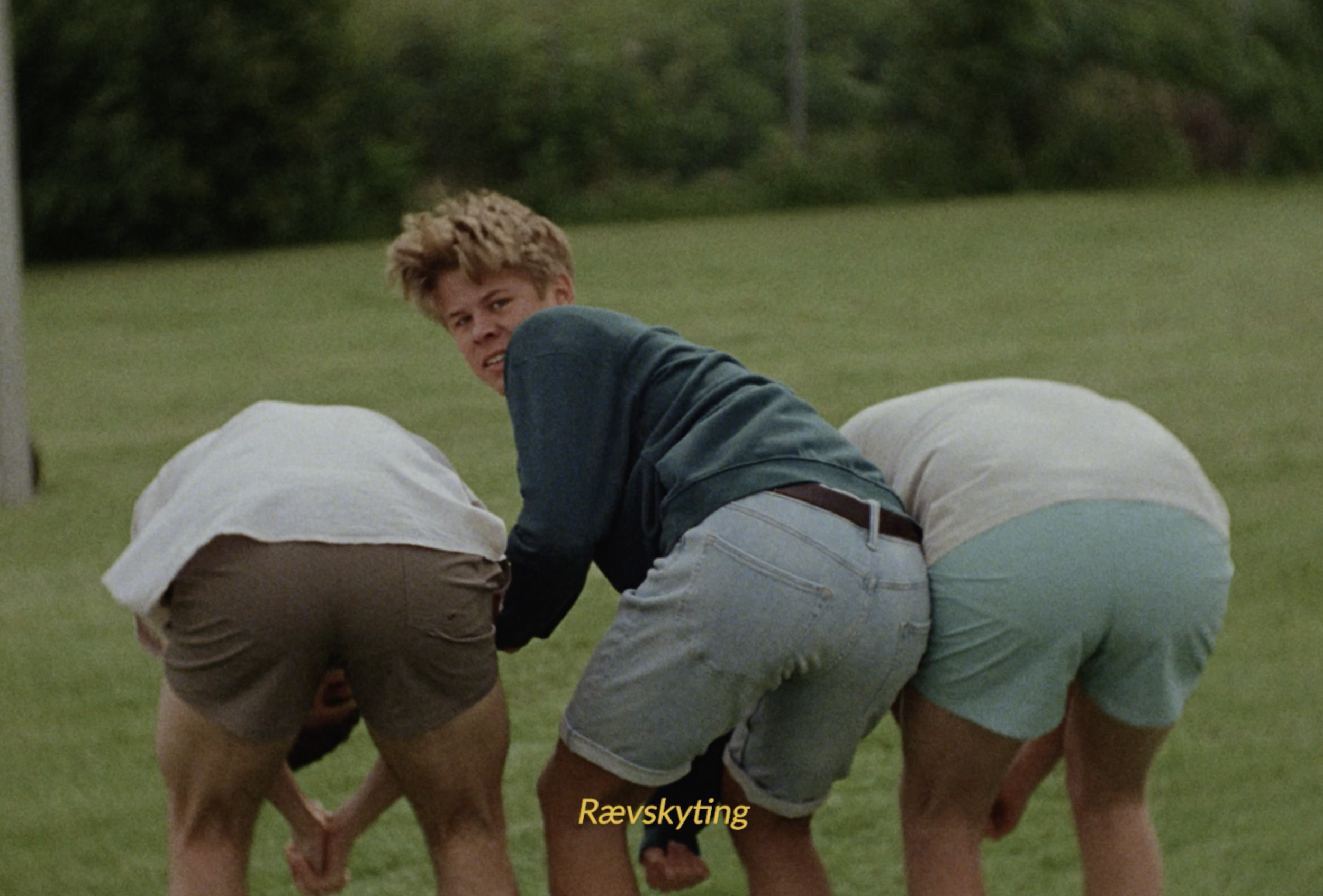 Three young people bending over on a grassy field in a Bama commercial still, cinematography by Johan-Fredrik Bødtker.