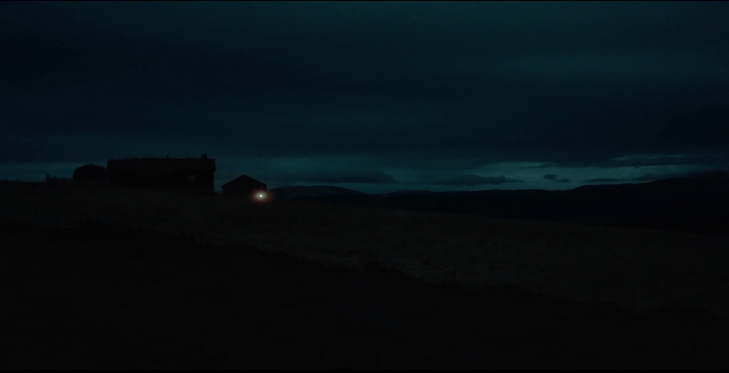 A dark, cloudy night with a silhouette of a house on a hill, a faint light glowing from a window, and rolling hills in the distance. fenris tv series