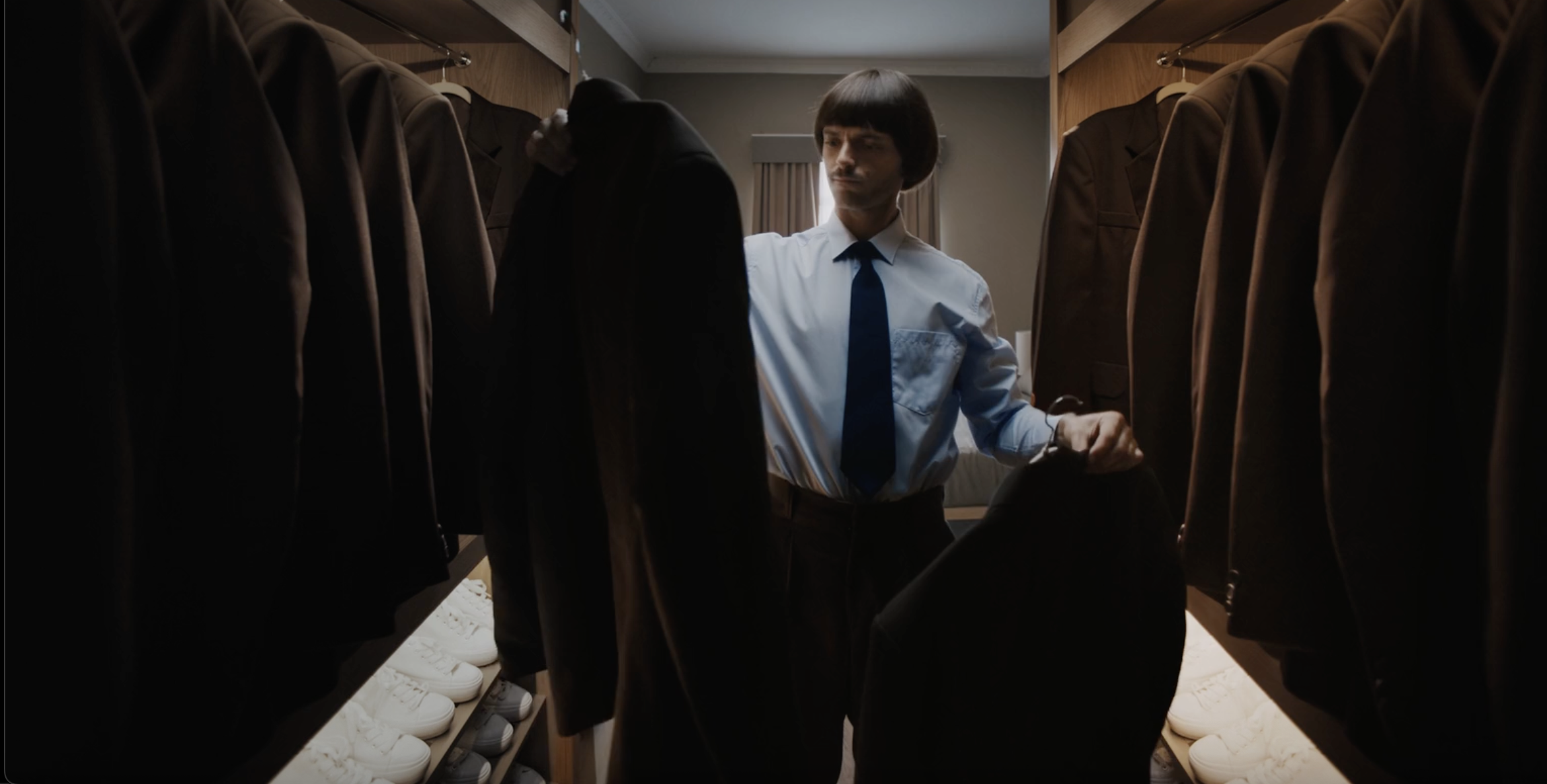 Man in a suit standing between hanging garments in a still from the CBOE commercial, cinematography by Johan-Fredrik Bødtker.