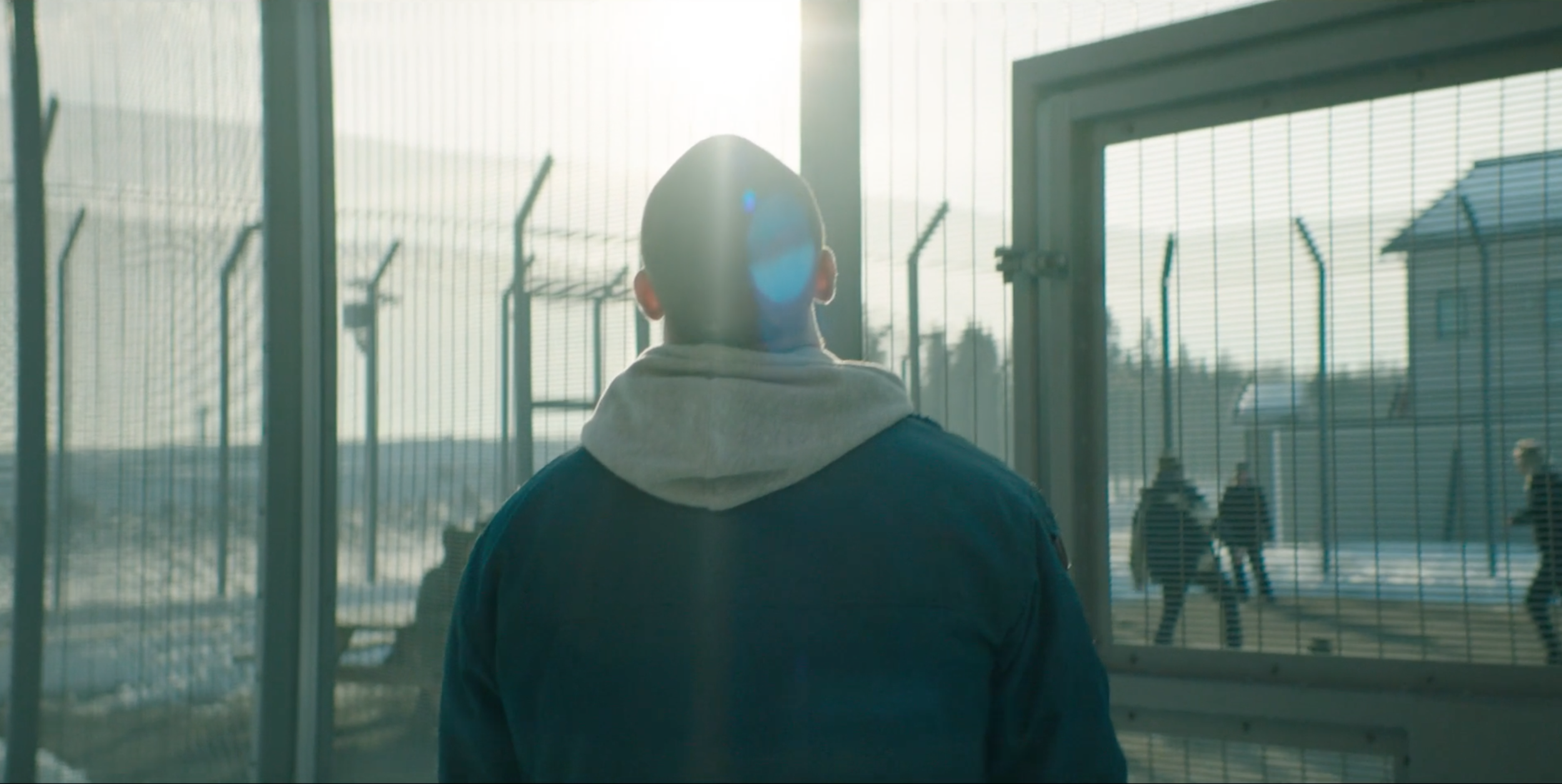 Man standing by a fenced prison area in Valkyrien, cinematography by Johan-Fredrik Bødtker.