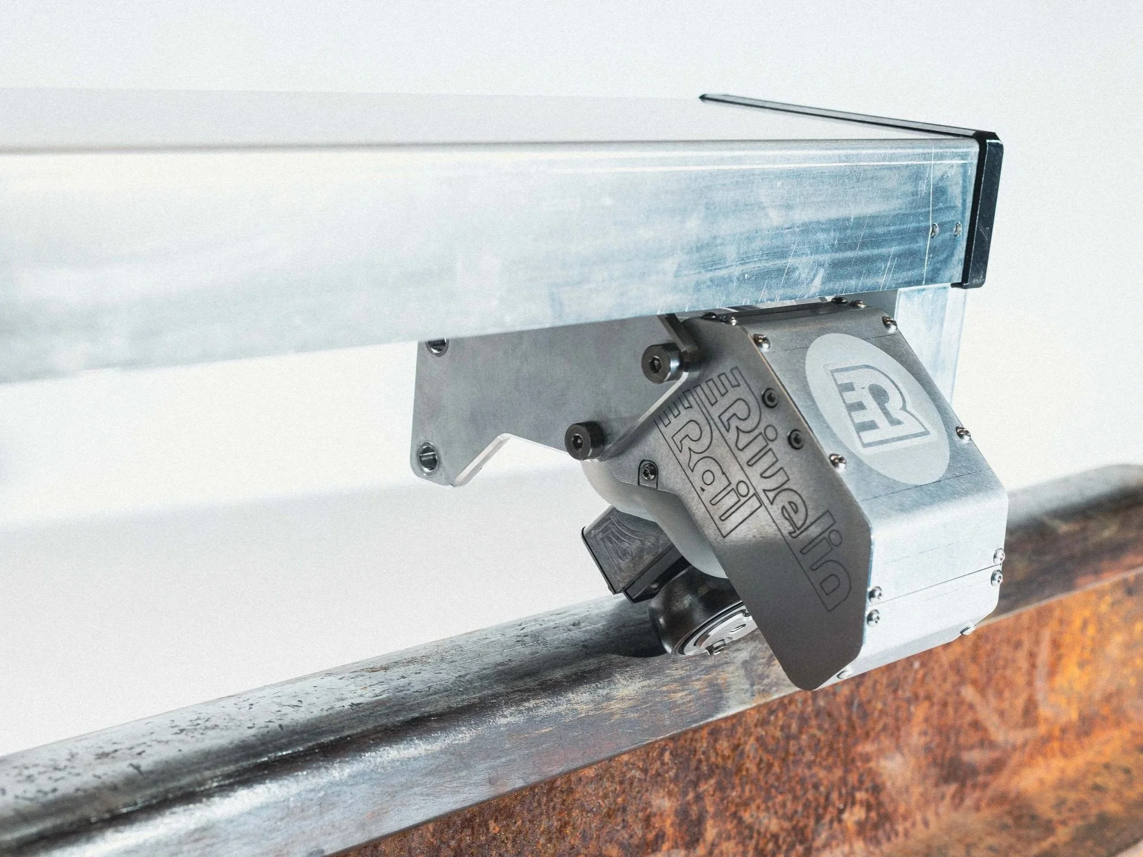 Close-up of a robotic arm with a metal surface, attached to a gray joint mechanism, positioned on a rust-colored metal surface.