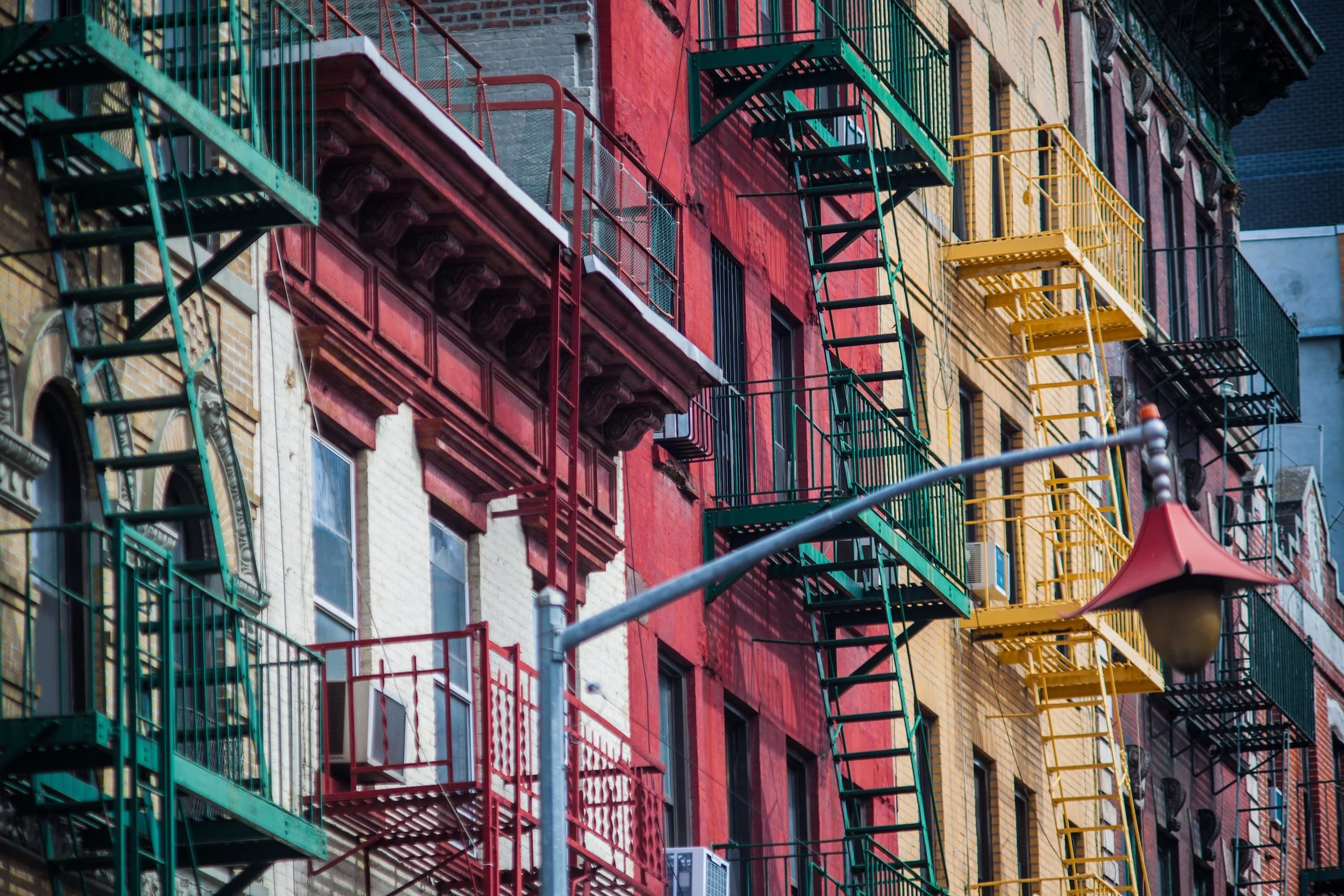 Colorful apartment building with red, yellow, and gray brick walls, multiple fire escapes, and a street lamp in the foreground.