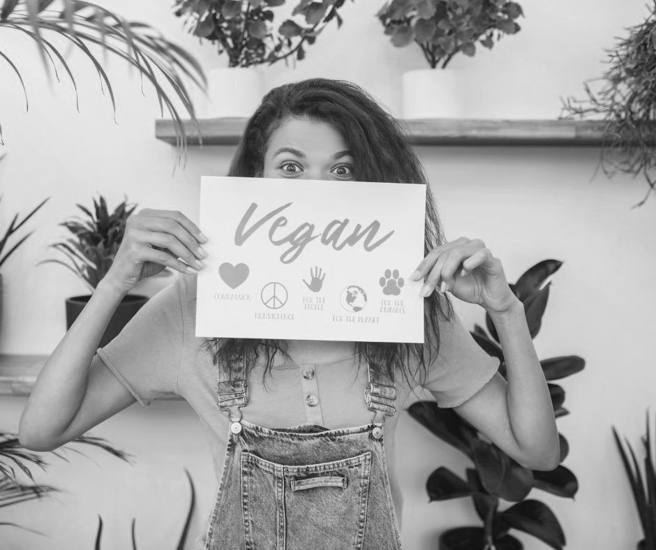Black and white image displaying a girl holding a paper with the word "vegan" on it.