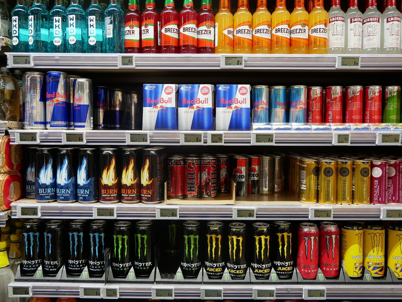 Store shelf filled with colorful energy drinks, including Red Bull, Monster, and others. Variety of brands and flavours attractively displayed.