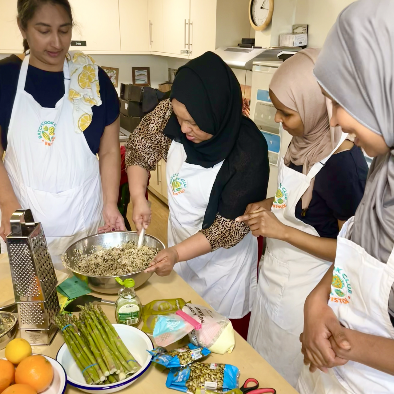 Three parents cooking together at Redcliffe Nursery school, smiling at the camera