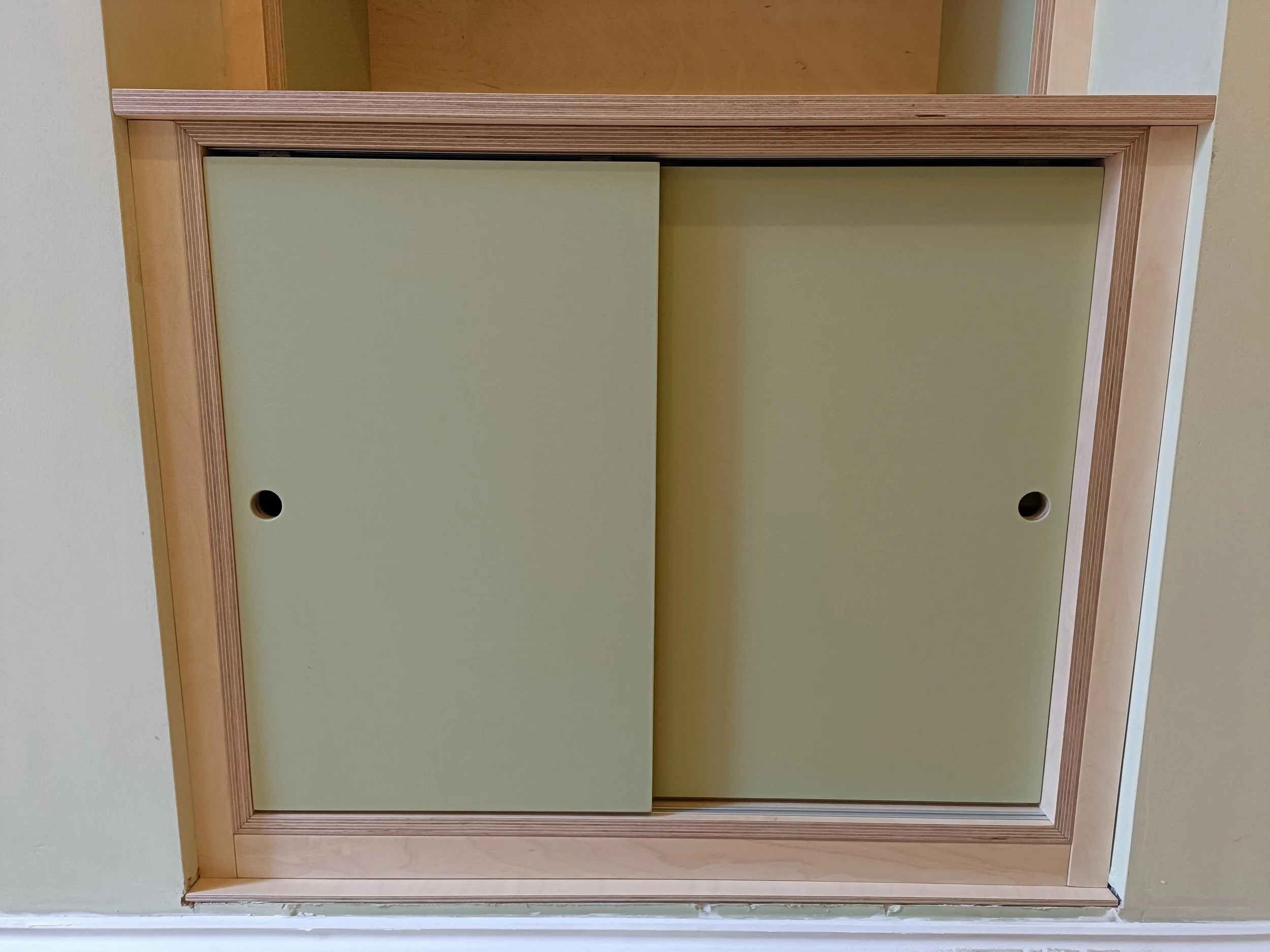Birch ply unit with painted elements and sliding doors installed into a small fireplace alcove in Heaton. 
