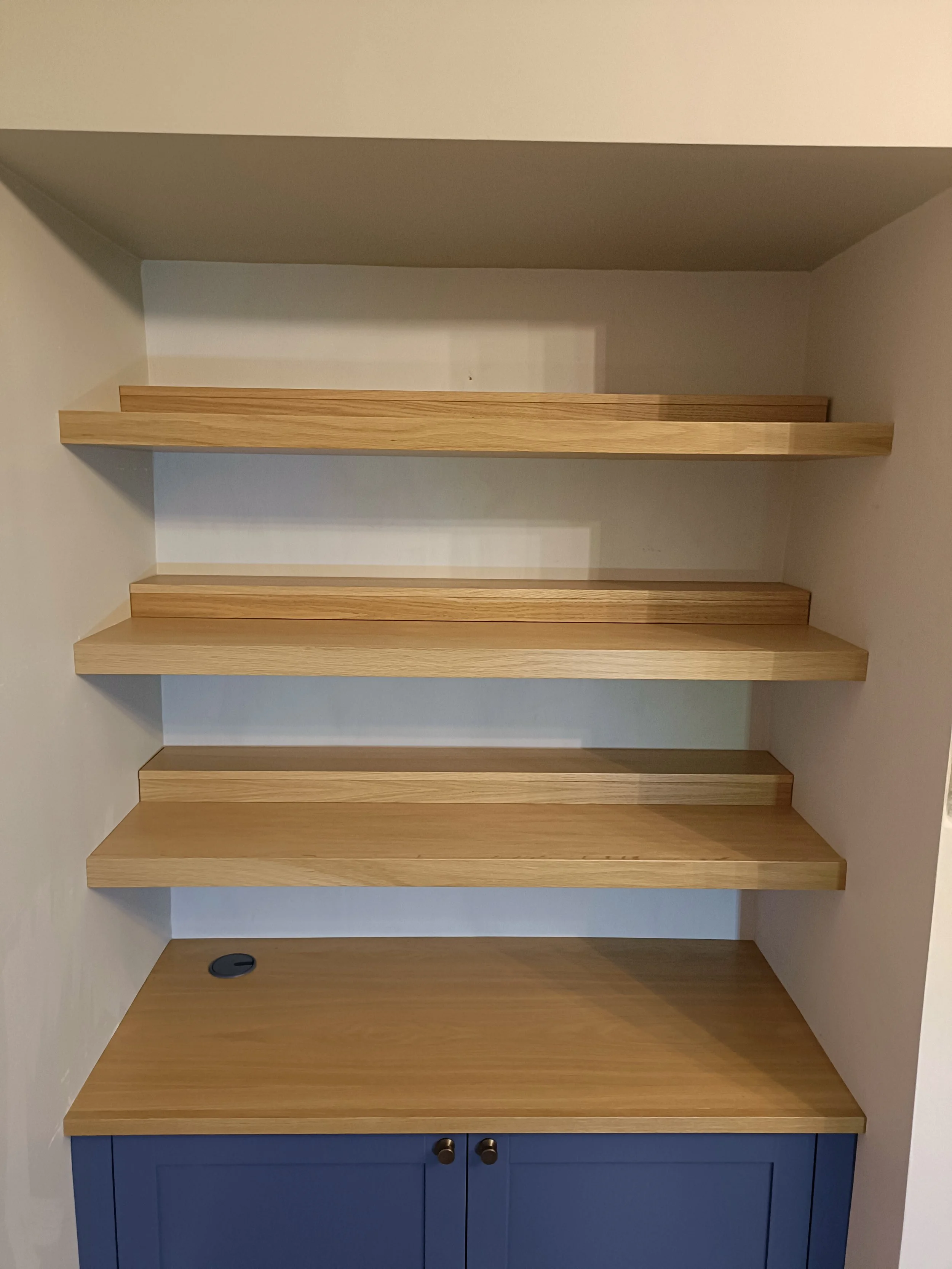An alcove cabinet with floating shelves above in a mix of painted finish and oak, installed in Gosforth. The oak floating shelves are extra deep and have additional removable 'lifts' at the back to allow the display of a double row of paperback books