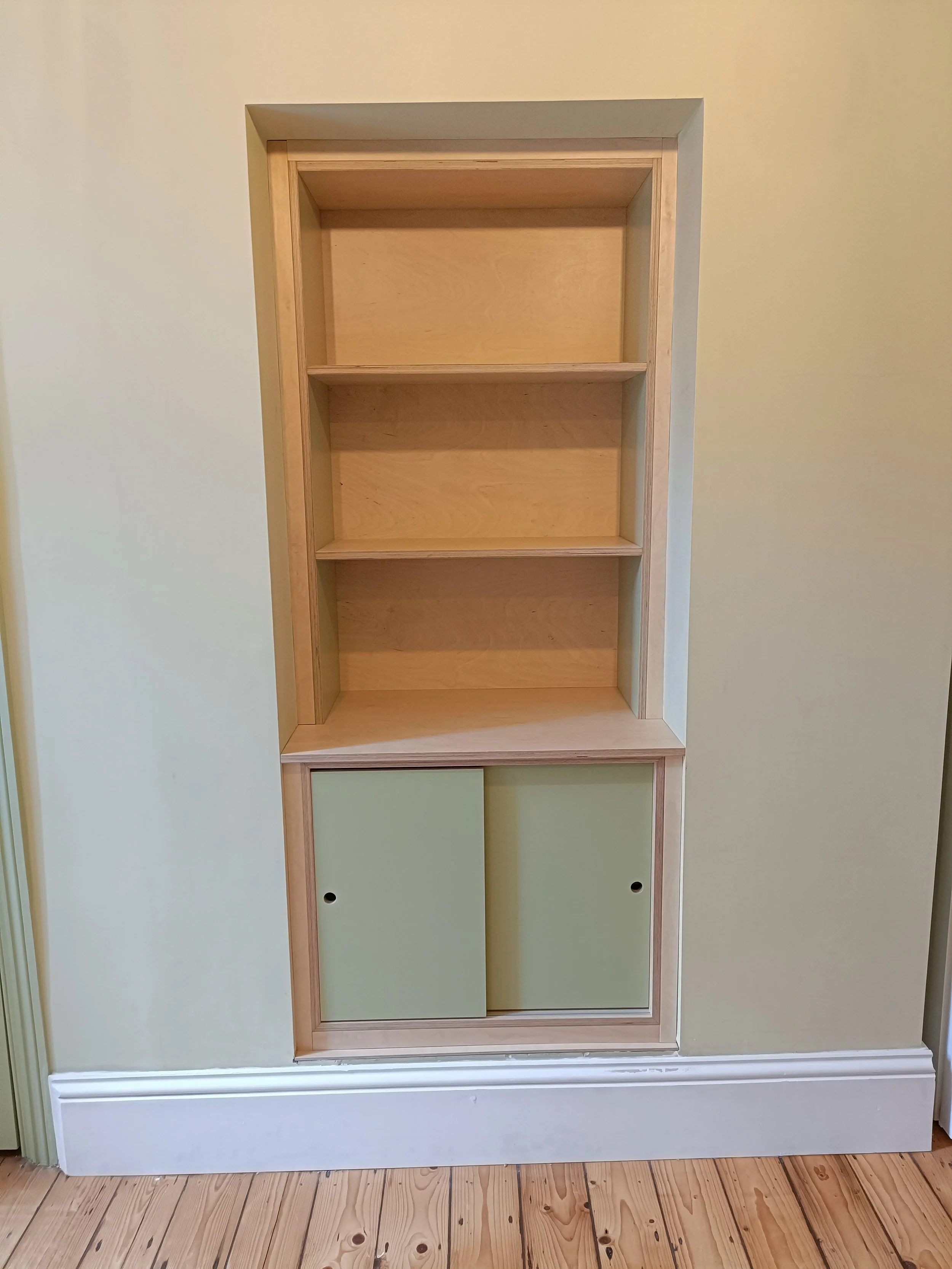 Birch ply unit with painted elements and sliding doors installed into a small fireplace alcove in Heaton. 
