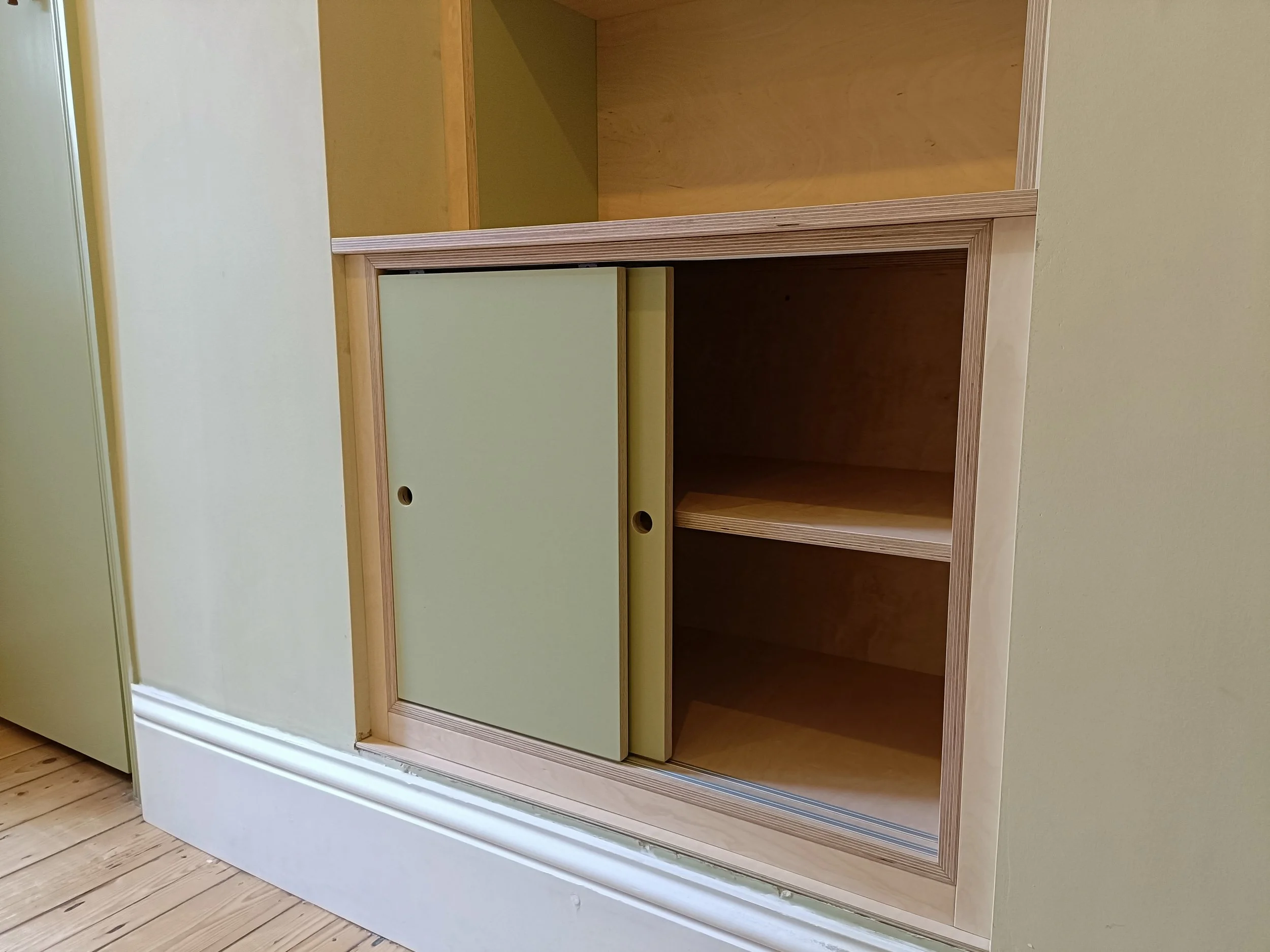 Birch ply unit with painted elements and sliding doors installed into a small fireplace alcove in Heaton. 