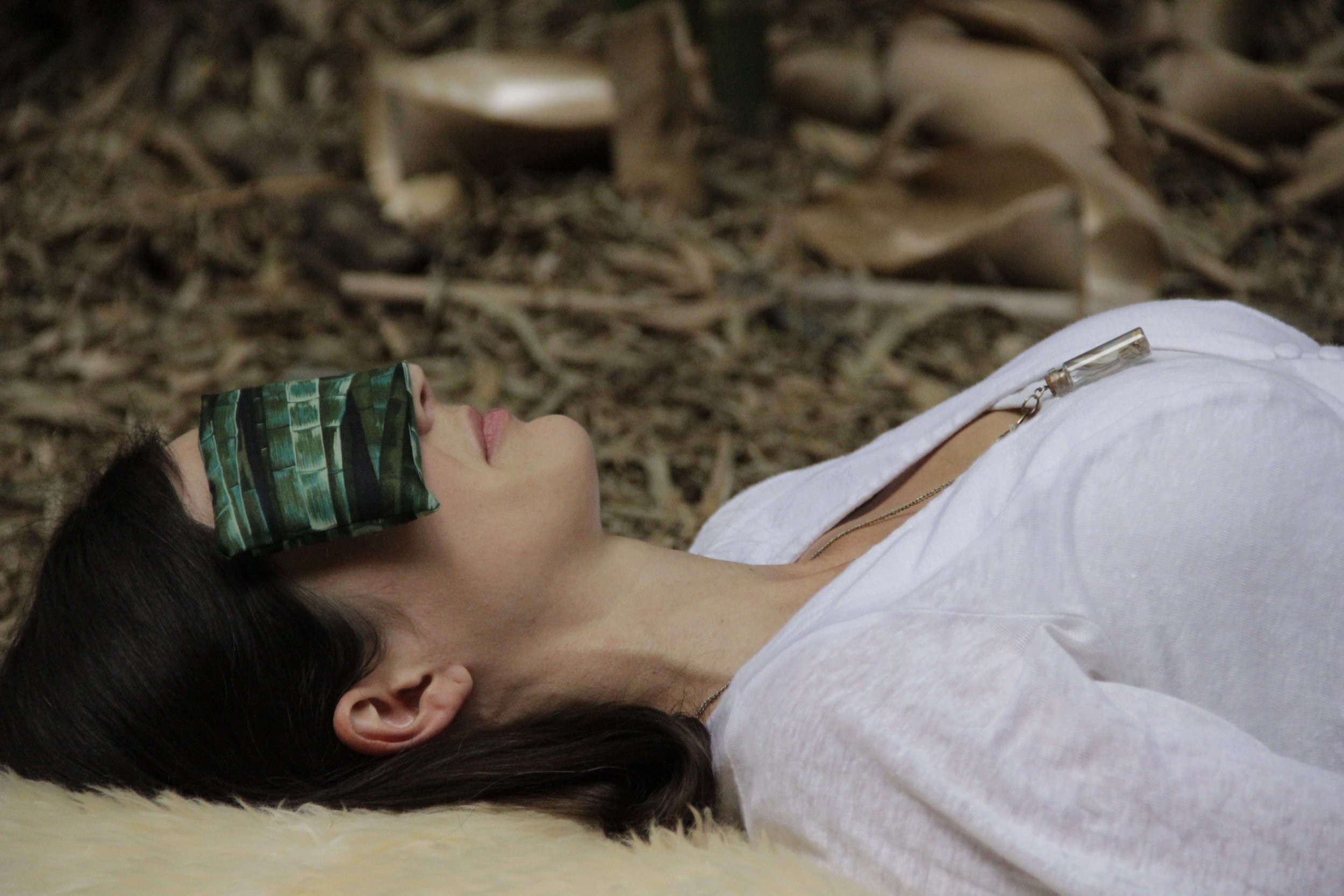A woman laying on her back in a bamboo forest practicing yoga nidra. She has a eye pillow over her eyes.