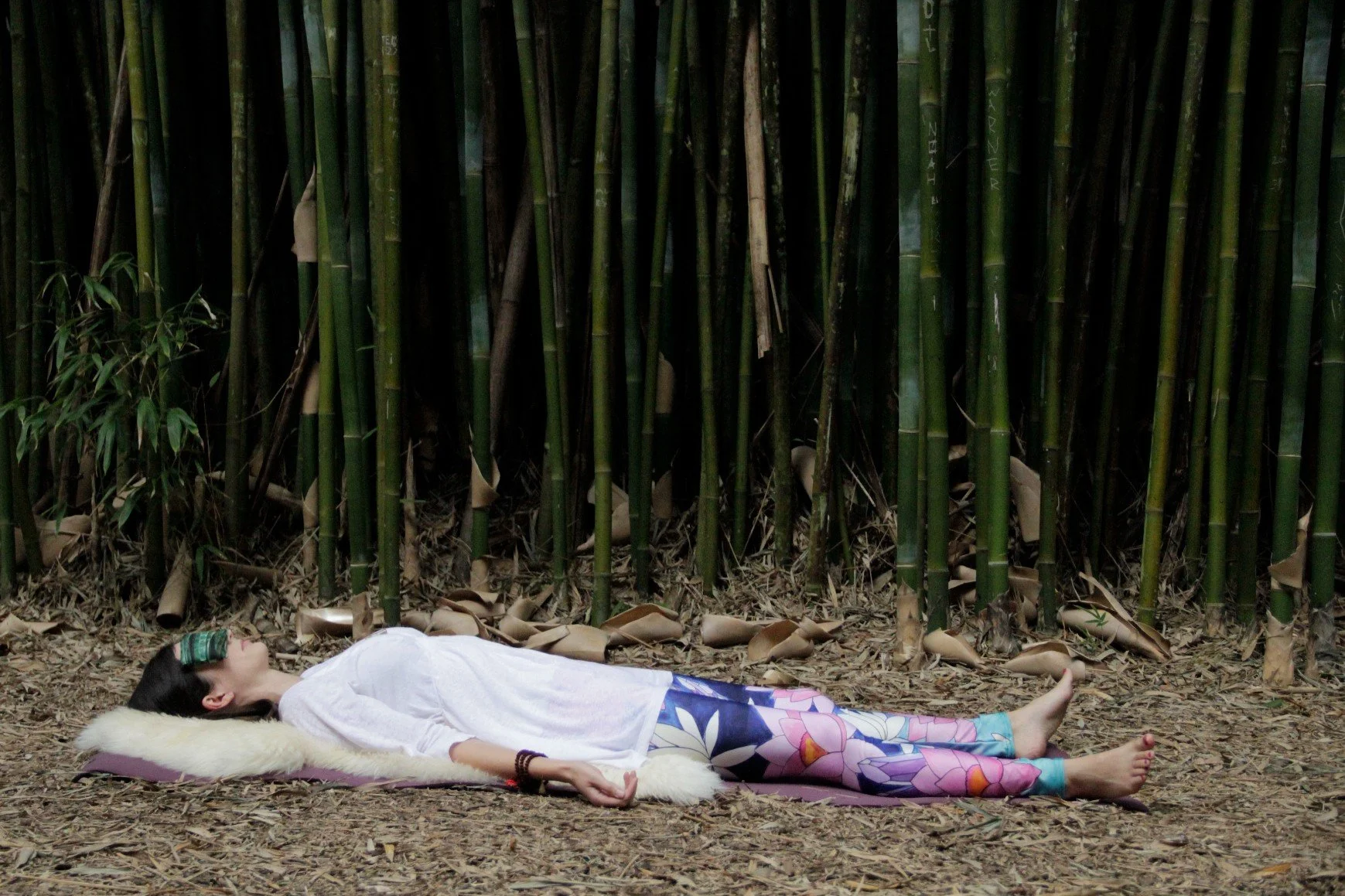 Woman lying on the ground in front of bamboo practicing yoga nidra