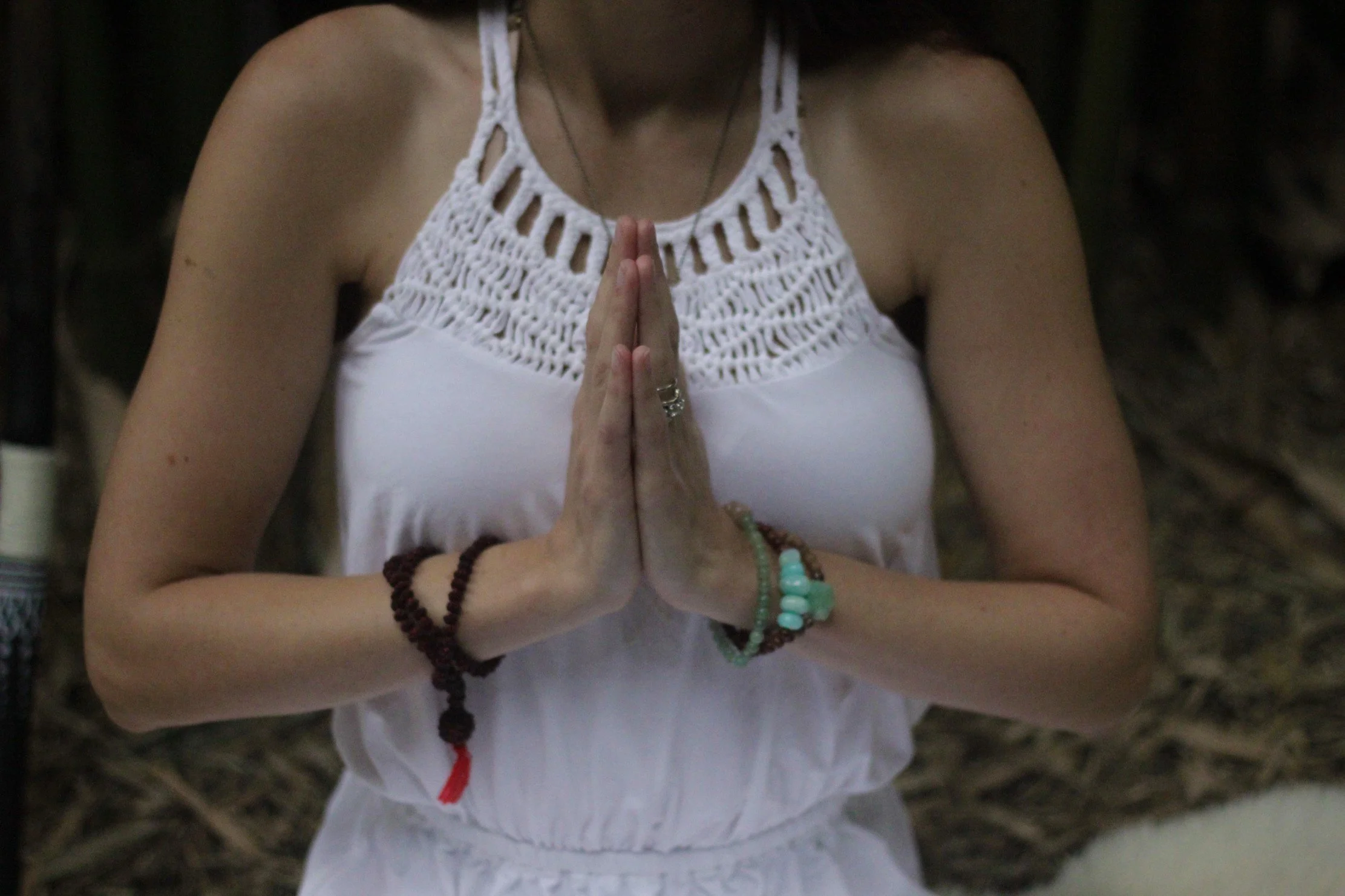 Woman wearing a white dress with her palms pressed together at her heart center.