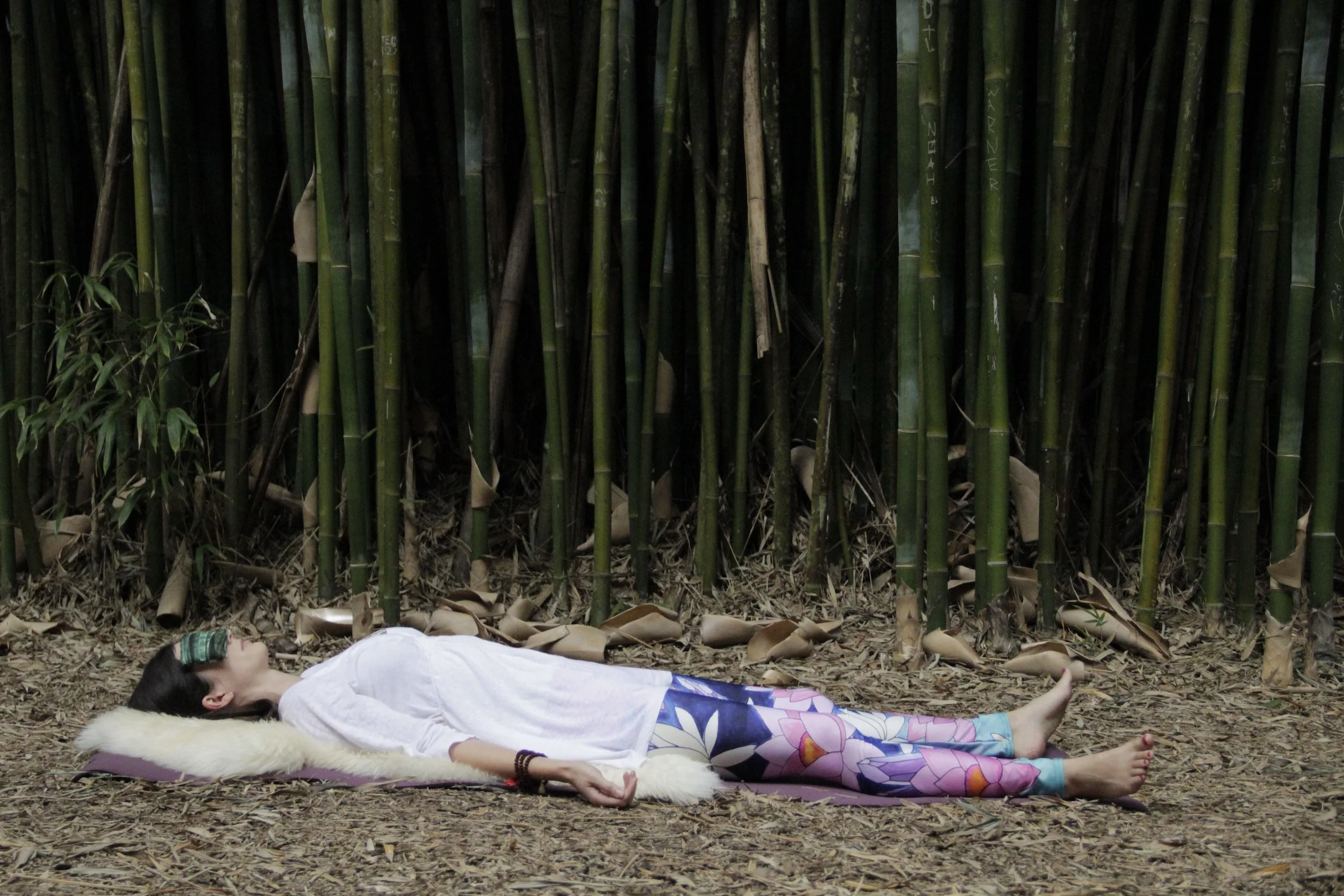 Woman lying in a bamboo forest practicing yoga nidra meditation.